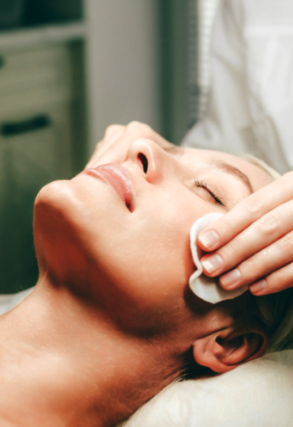 Delux Facial at MoonSun Esthetics - A woman receiving a facial cleansing treatment with a cotton pad at a spa or skincare clinic.