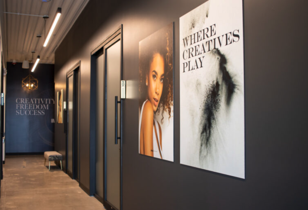 At MoonSun Esthetics - Hallway with dark walls, featuring a mural of a woman with curly hair and a large white sign with black text that reads "WHERE CREATIVES PLAY."
