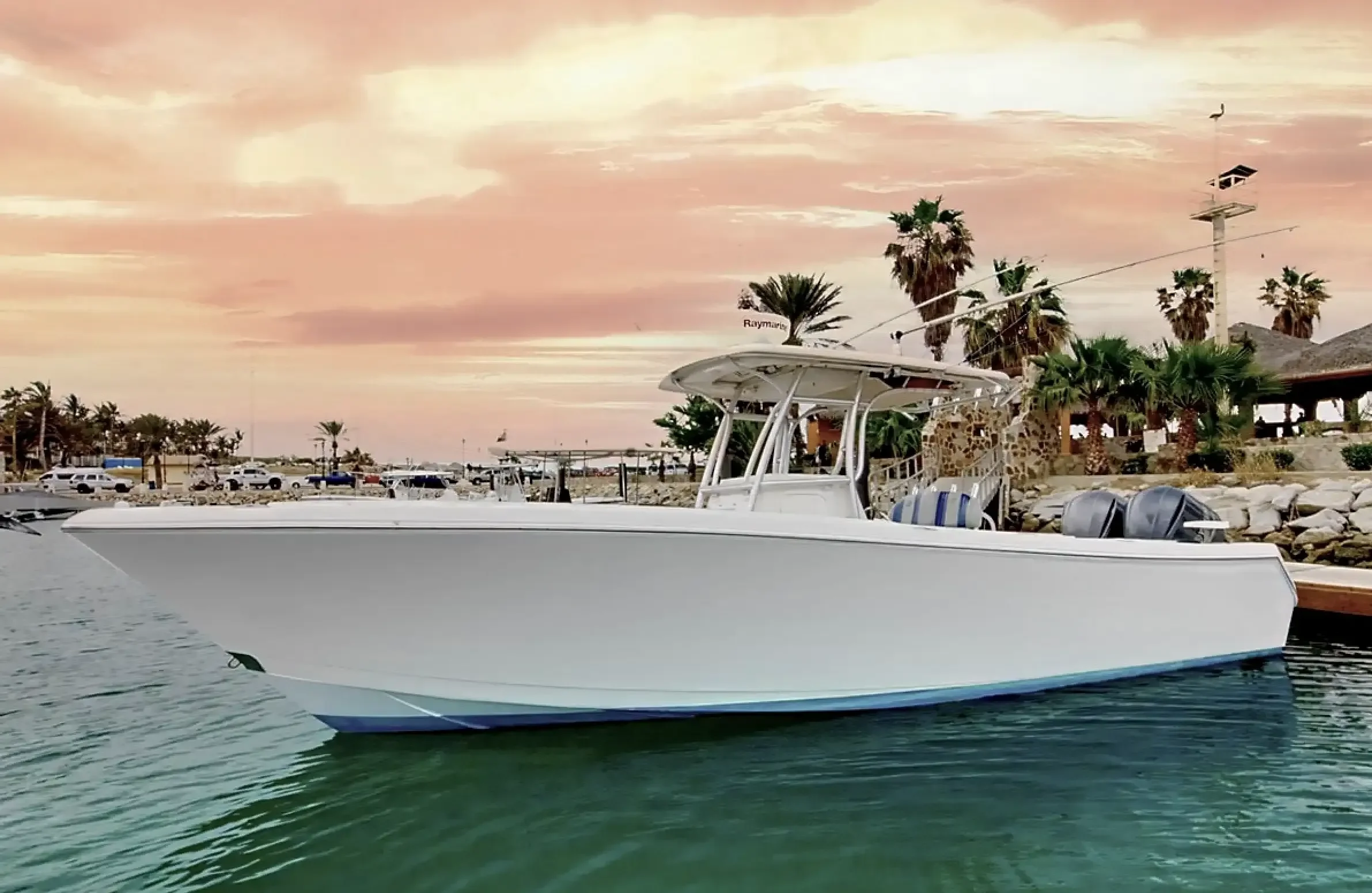 A white yacht docked in a marina with palm trees and a pink sunset sky in the background. Fishing San Jose del Cabo