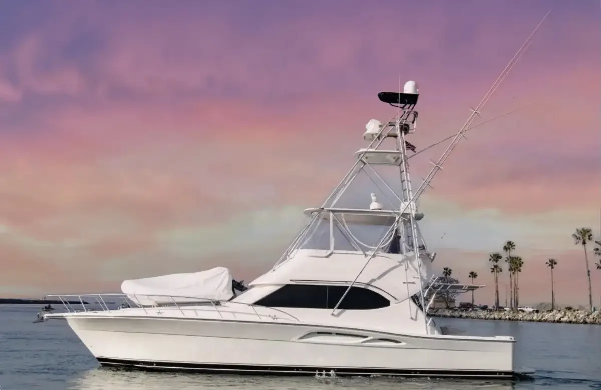 A white fishing yacht on calm water during sunset with a pink and purple sky, palm trees in the background. San Jose del Cabo fishing charters