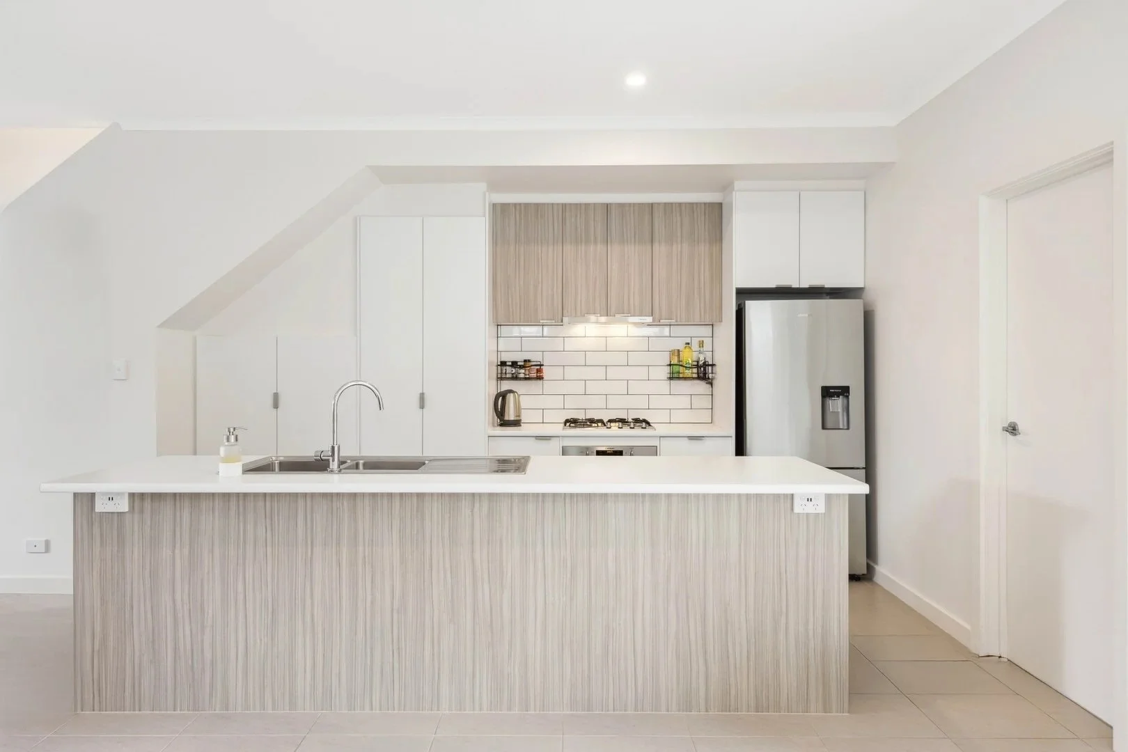 Modern kitchen with white and light wood cabinets, subway tile backsplash, stainless steel appliances, and a large island.