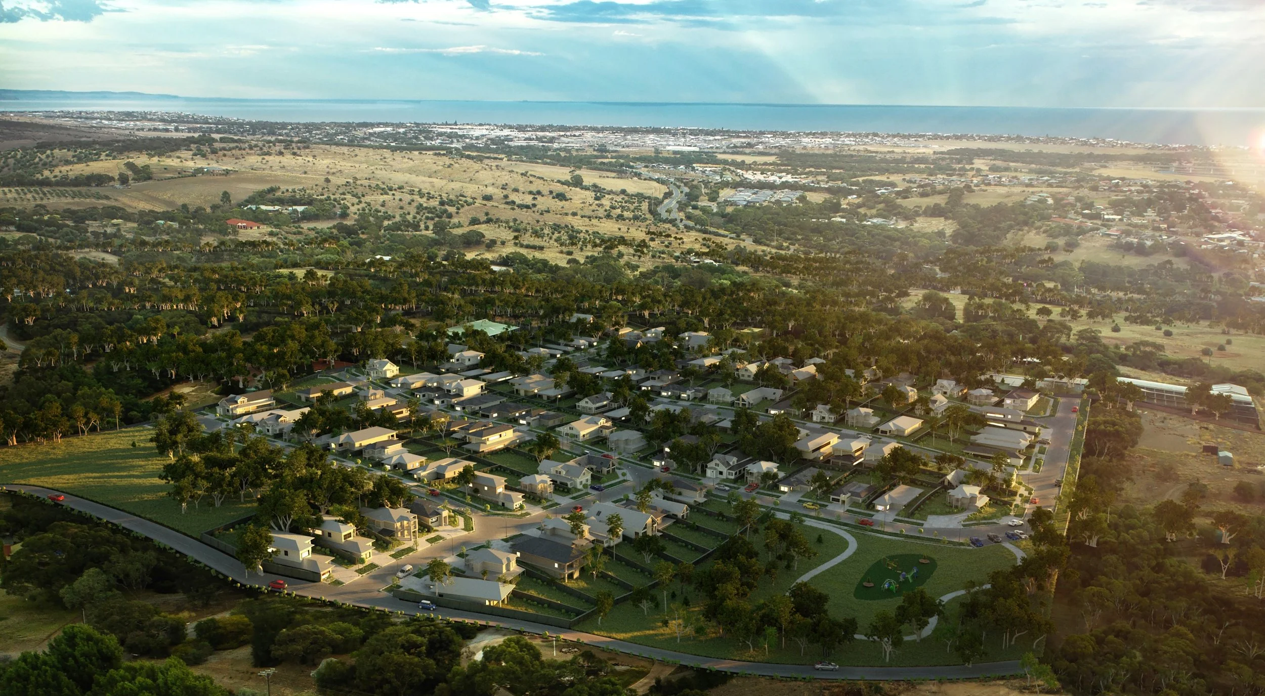Aerial view of a residential neighborhood with houses, trees, roads, and a park, overlooking a coastal area with water and distant shoreline in the background, during sunset.