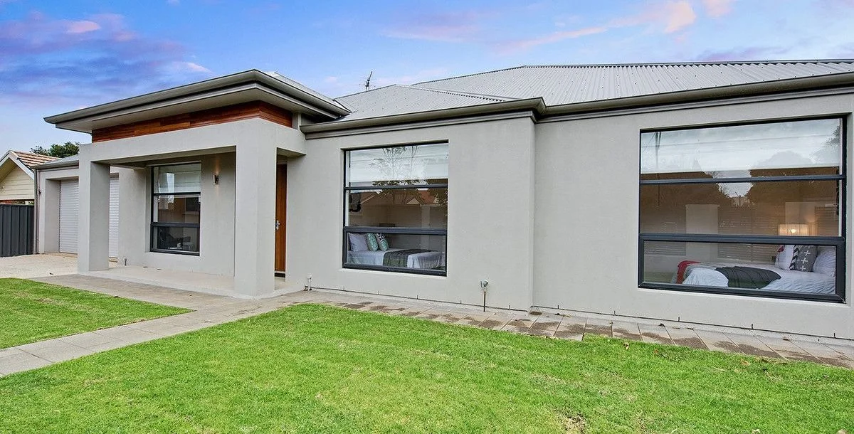 Front exterior of a modern house with large windows, a small porch, and a well-maintained lawn.