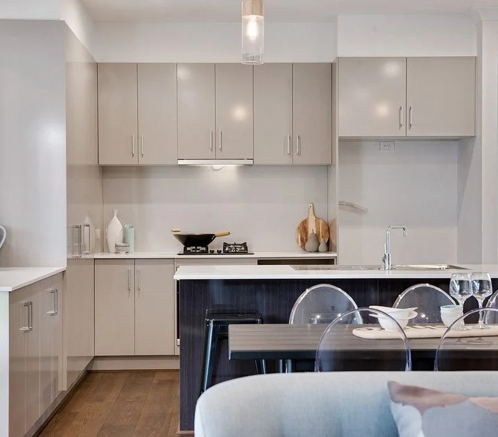 Modern kitchen with beige cabinets, a white countertop, a black stove, and a small dining table with transparent chairs.