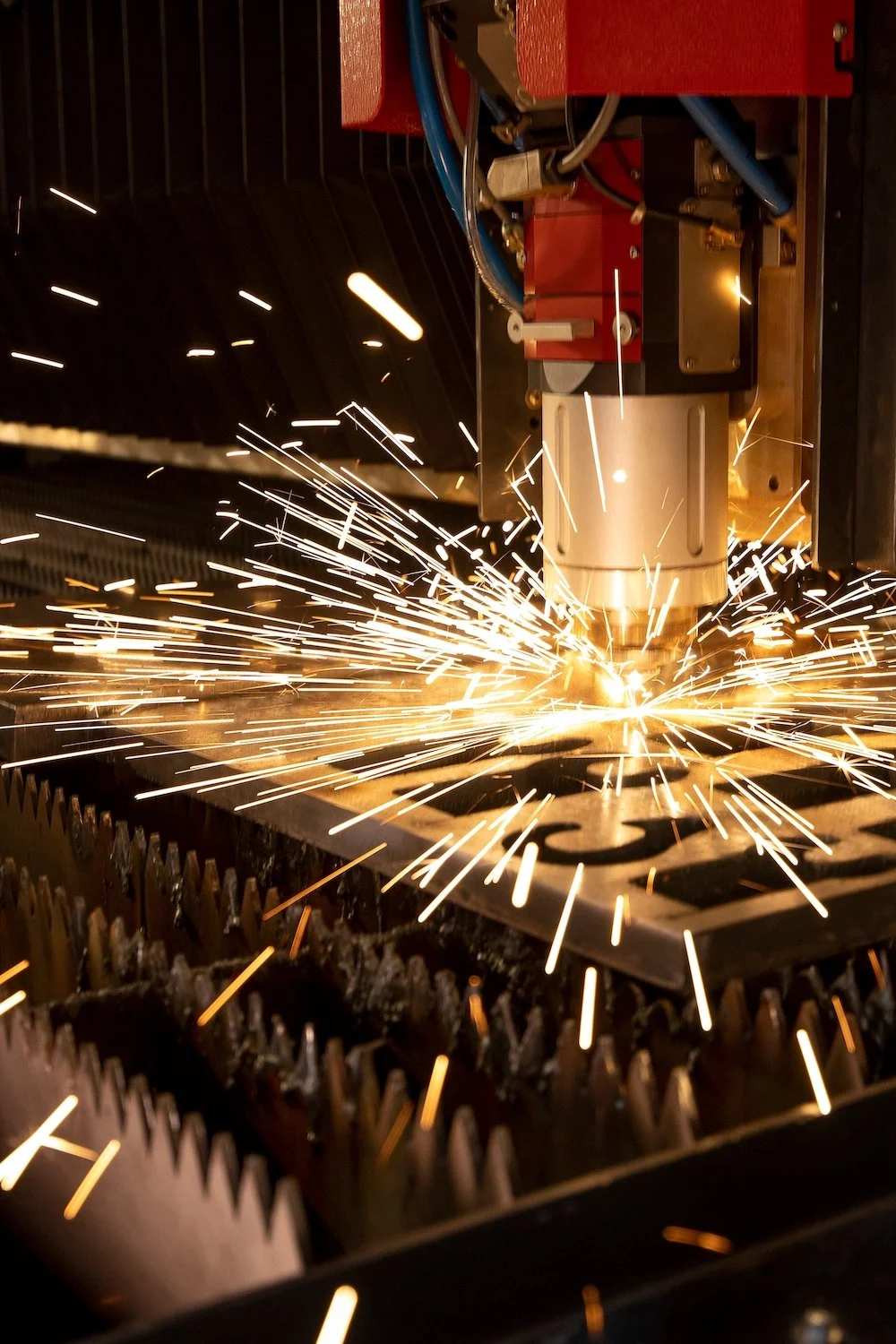 A laser cutting machine is cutting metal with sparks flying, inside an industrial workshop.