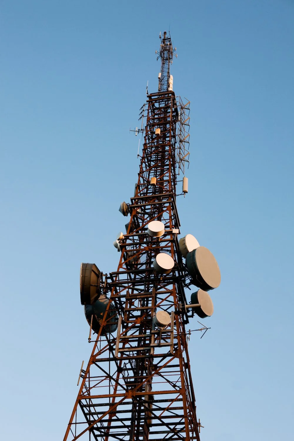 A tall metal communications tower with various antennas and satellite dishes against a clear blue sky.