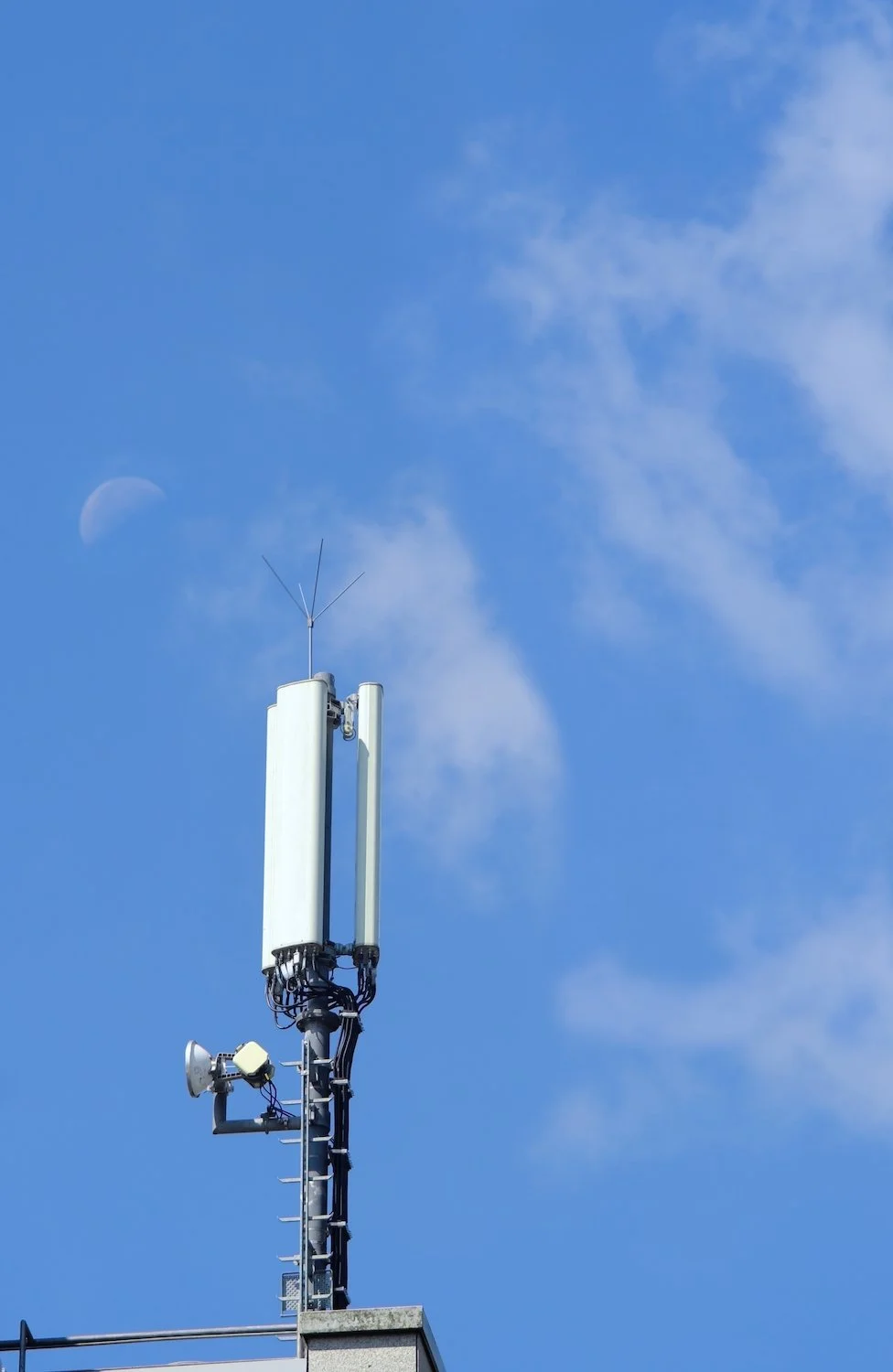 A telecommunications tower with antennas and a loudspeaker against a blue sky with clouds and a visible moon.