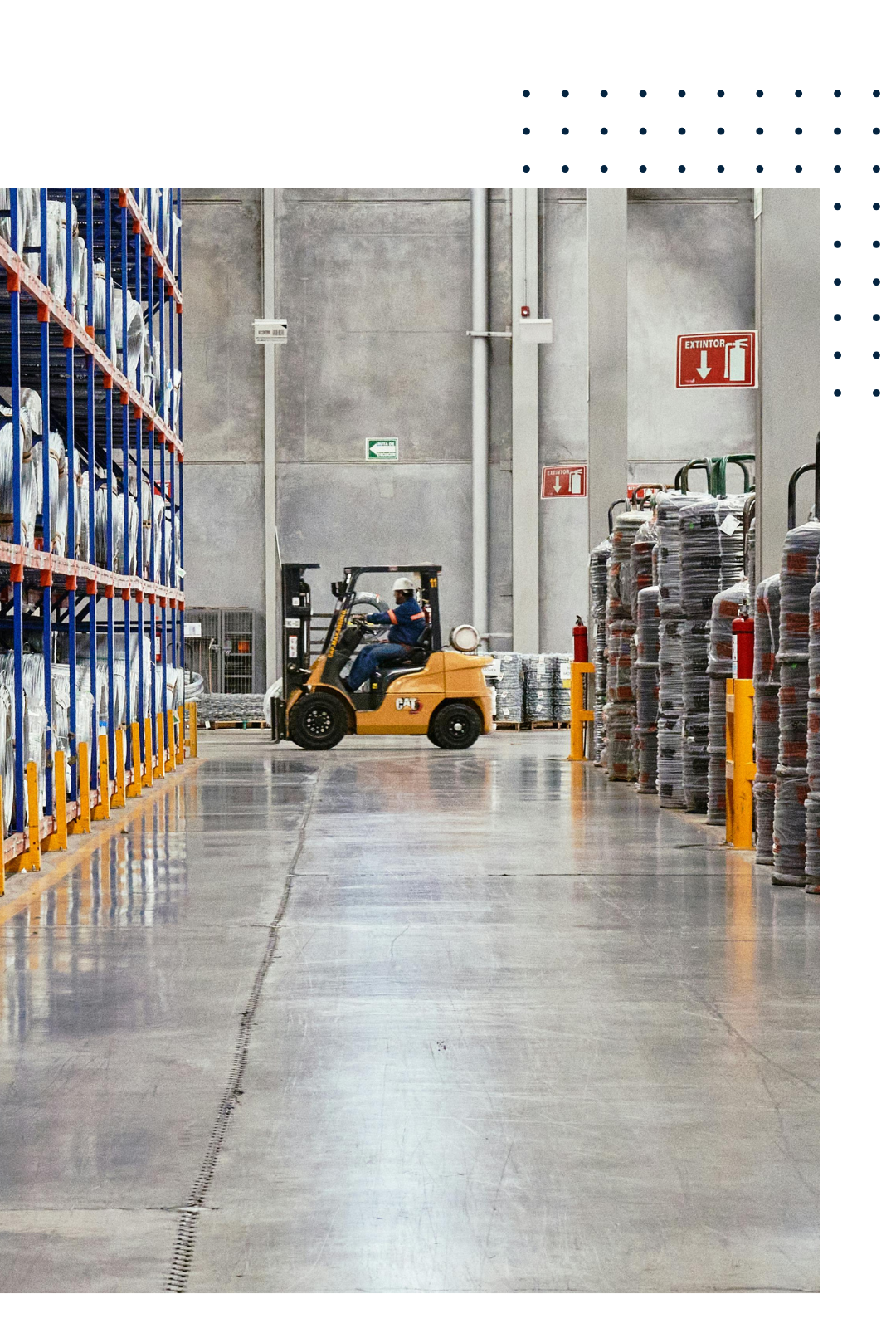 A warehouse with shelves stocked with large white bags, a forklift operator driving a yellow CAT forklift, and stacks of wrapped pallets. The warehouse has a concrete floor, industrial walls, and safety signs including fire extinguishers and exit signs.