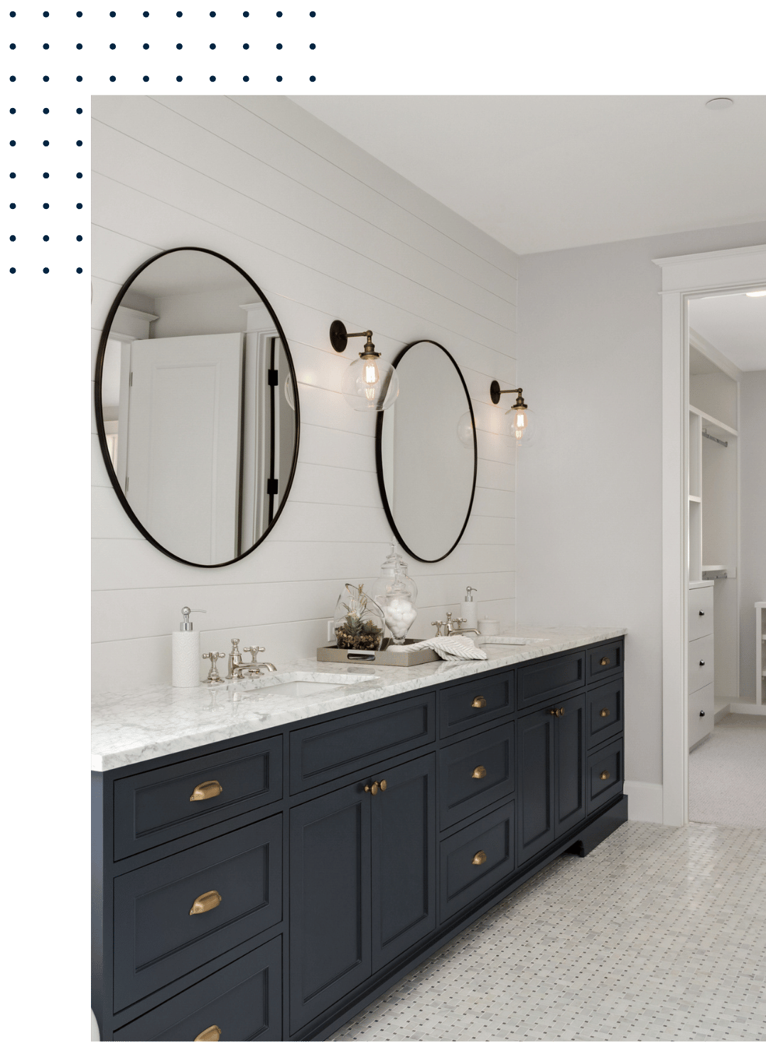 Modern bathroom with dark blue vanity, white marble countertop, two oval mirrors, and wall-mounted light fixtures.