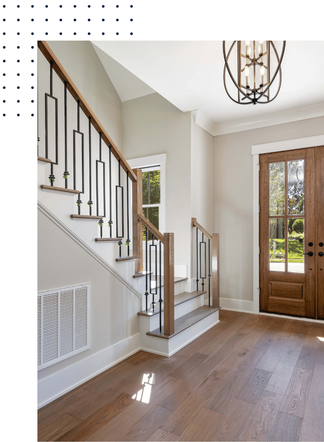 Interior entryway with wooden staircase and black metal railing, wooden front door with glass panels, hardwood floor, and a modern chandelier ceiling light.