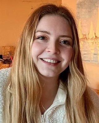 A young woman with long blonde hair smiling in an indoor setting.