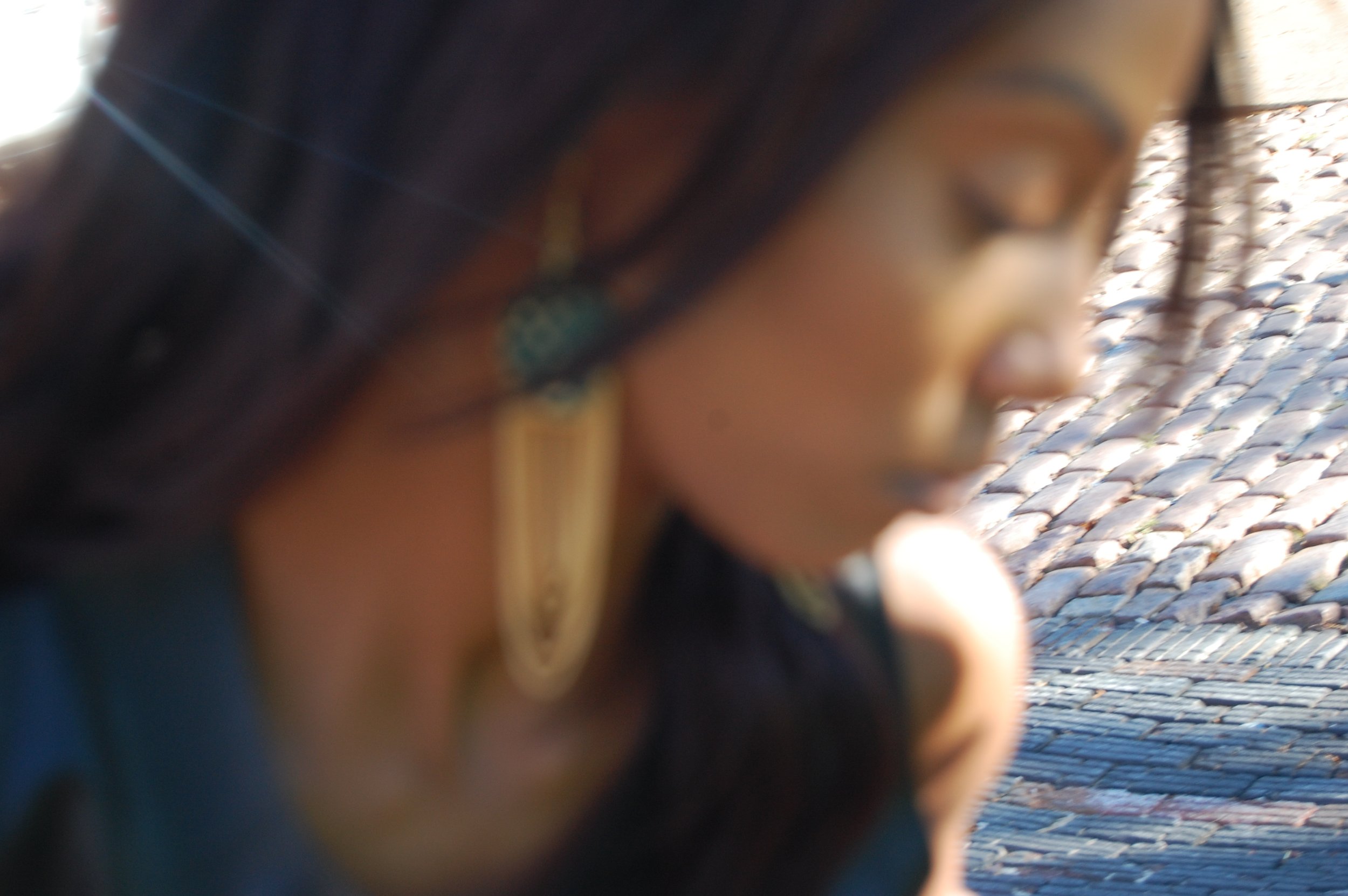 A close-up, blurry photo of a woman wearing large earrings and dark hair, with a textured tiled roof in the background.