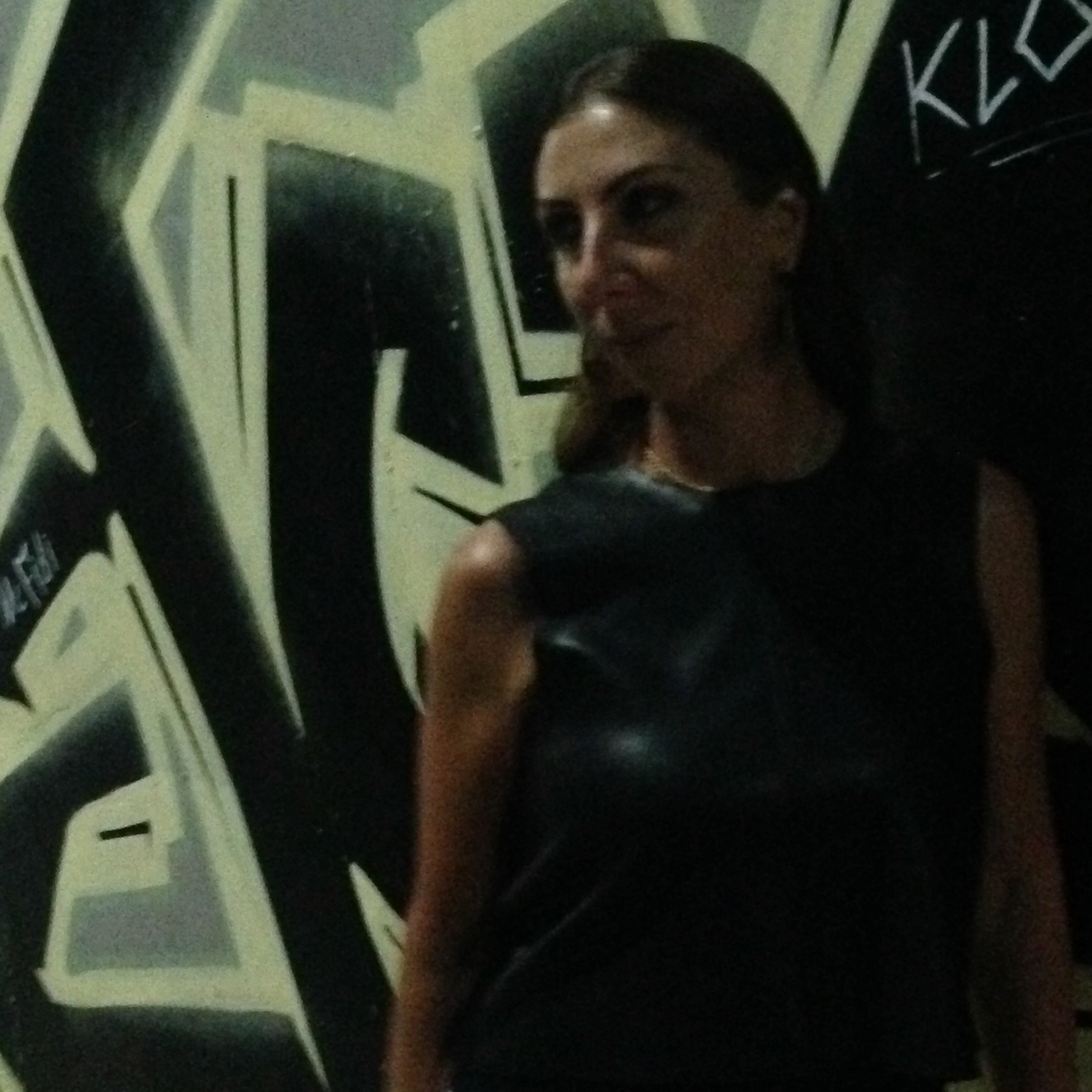 Artist Magda Parasidis standing near graffiti-covered wall at night.