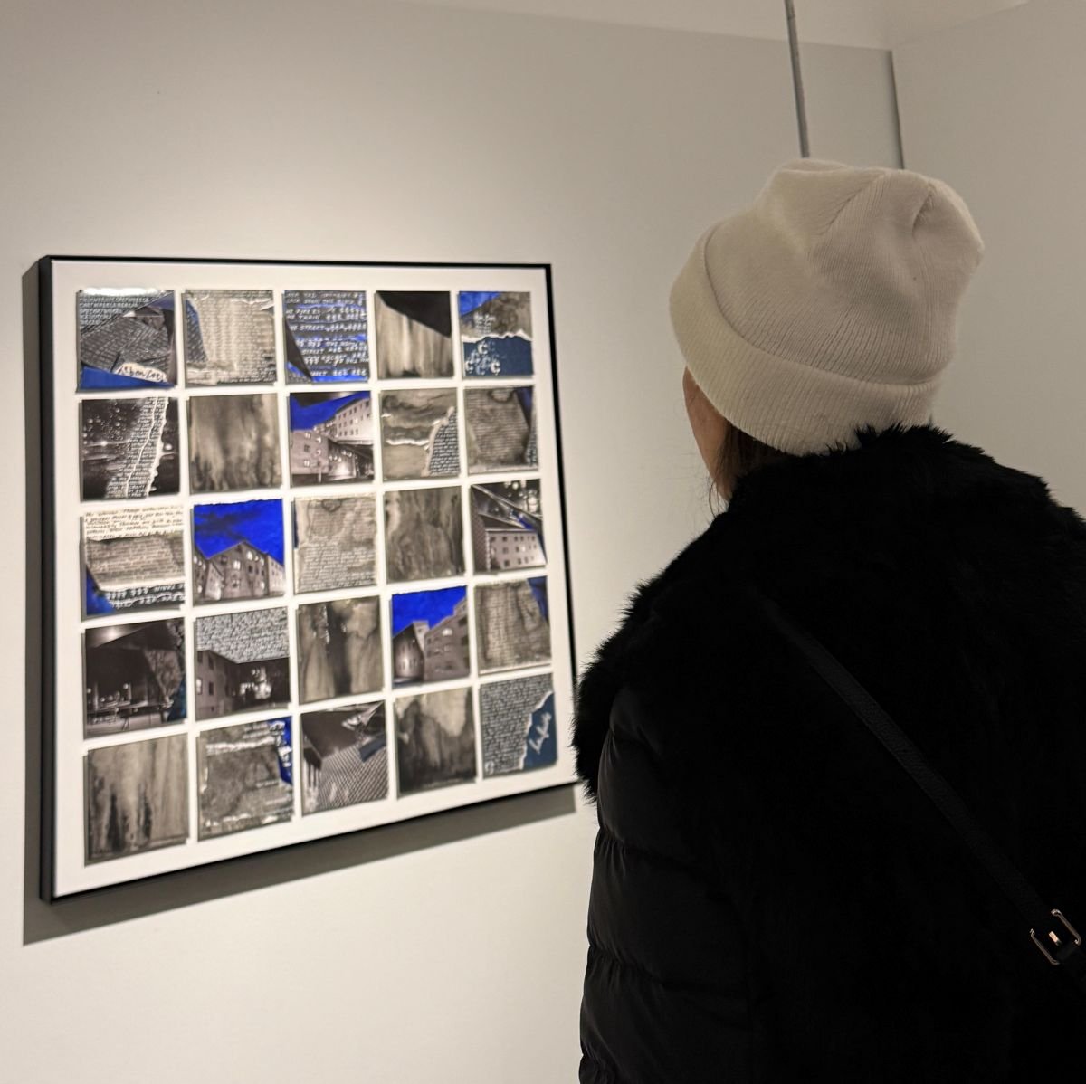 Magda Parasidis at Urban Arts Space Columbus OH OSU Ohio State Artist Commune Kite exhibition observing a framed collage of black and white photographs and some with blue accents, displayed on a gallery wall.