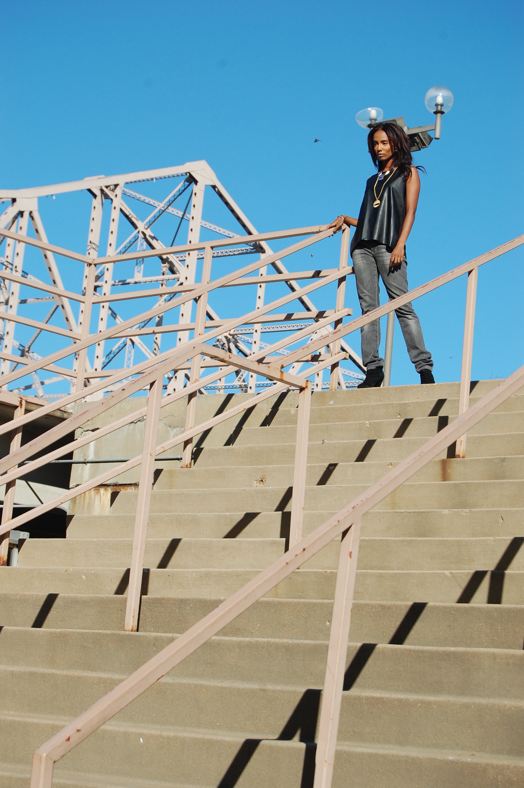A woman standing on top of a staircase with a skateboard in her hand, near an old structure with a blue sky in the background.