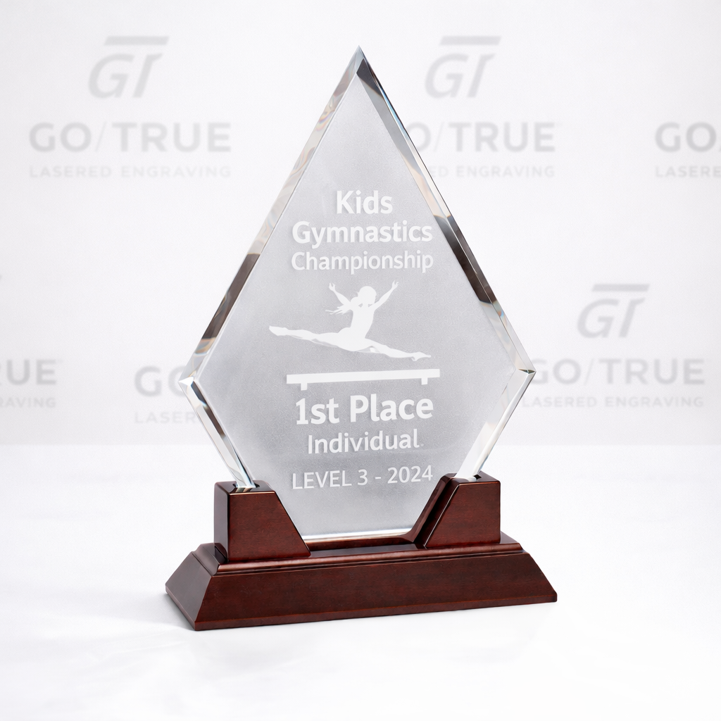 A clear glass trophy with a wooden base, engraved with an image of a gymnast, and text indicating 1st place in a kids gymnastics championship in 2024.