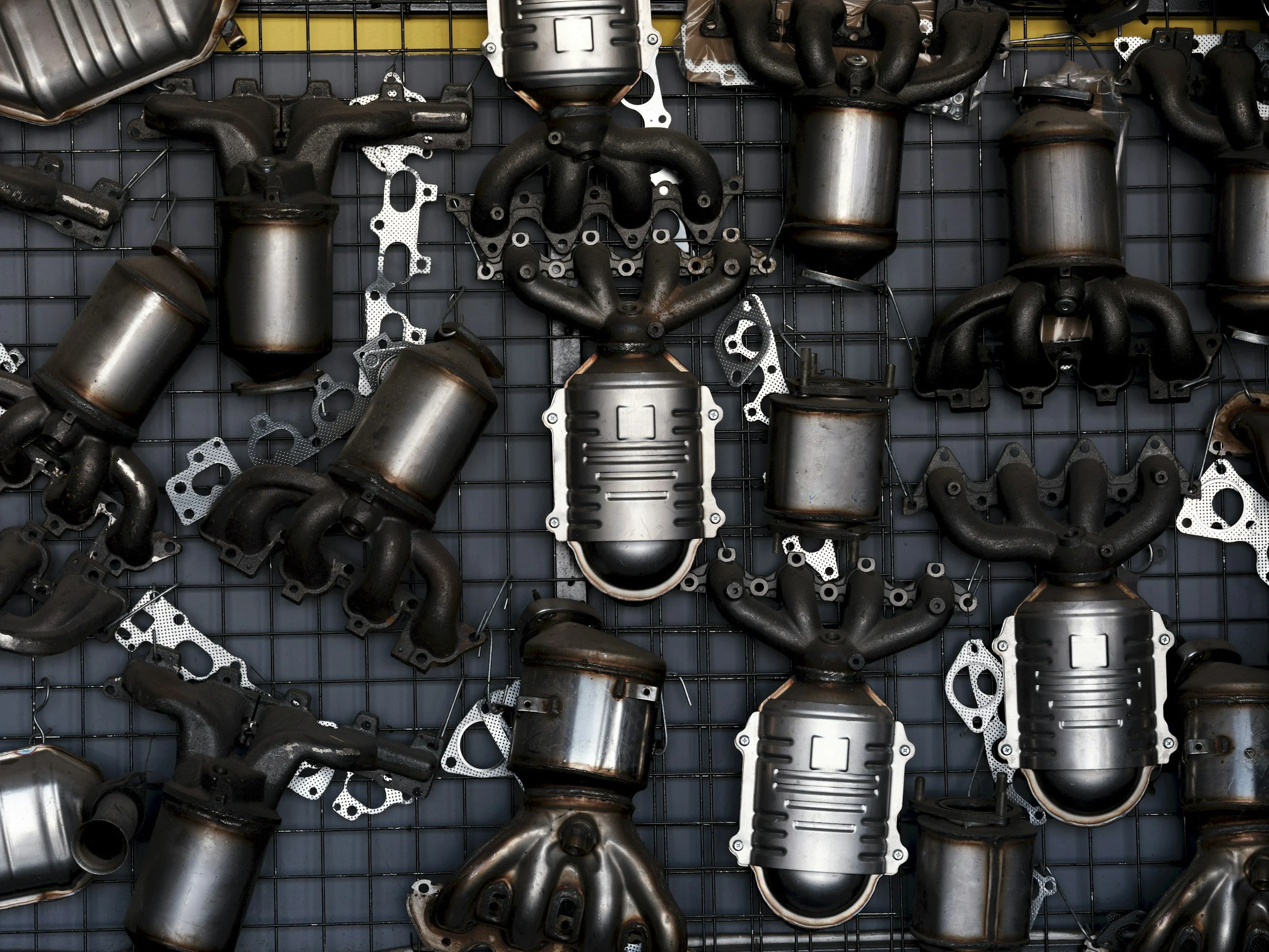 A display of various automotive exhaust parts and gaskets mounted on a wire grid display. The parts include exhaust manifolds, catalytic converters, and various gaskets.