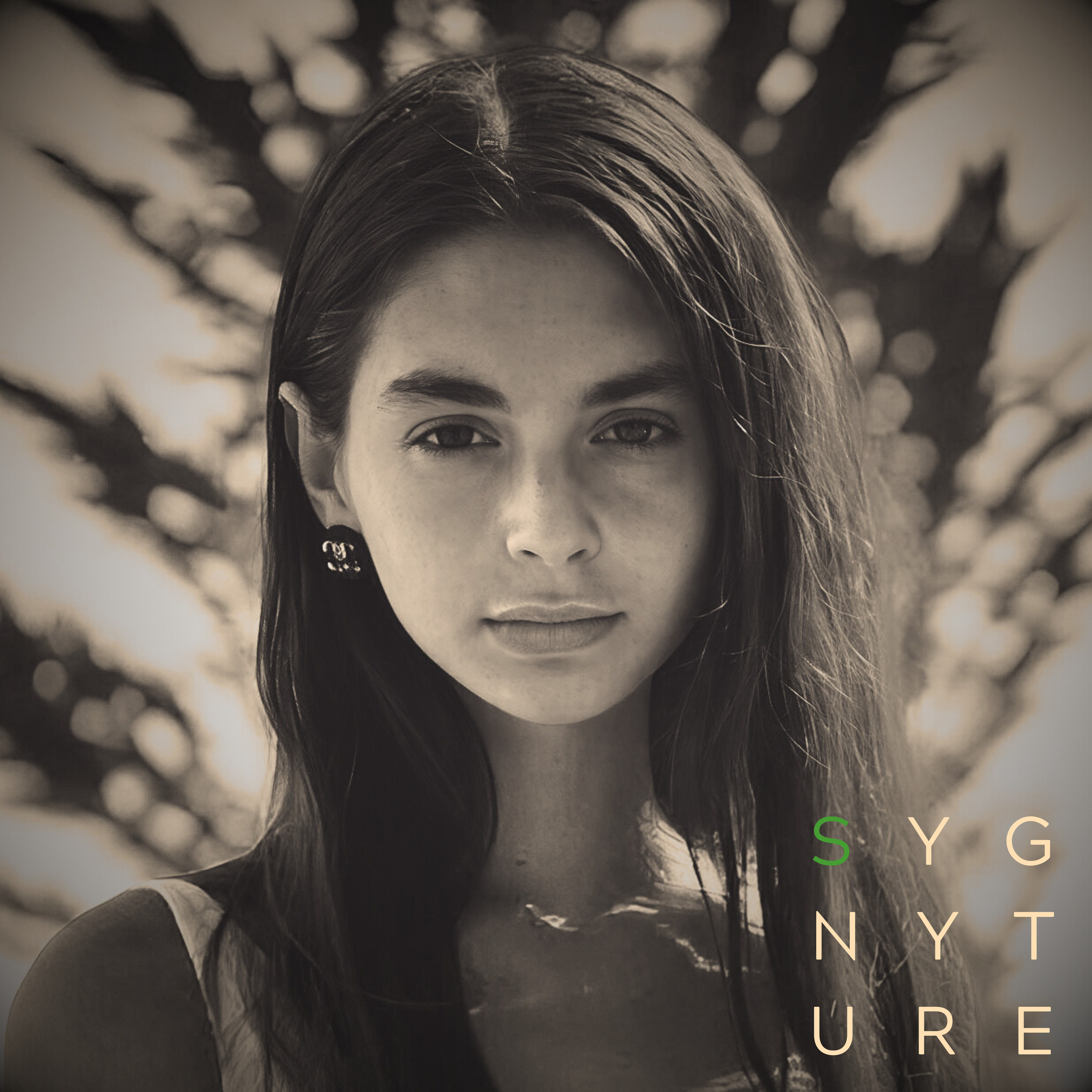 Close-up black and white photo of Mackenzie Shirilla's face with long hair and expressive eyes, with out-of-focus bokeh background. Overlay SYGNYTURE stamp. 'S' in green the rest of the letters in a light tan.