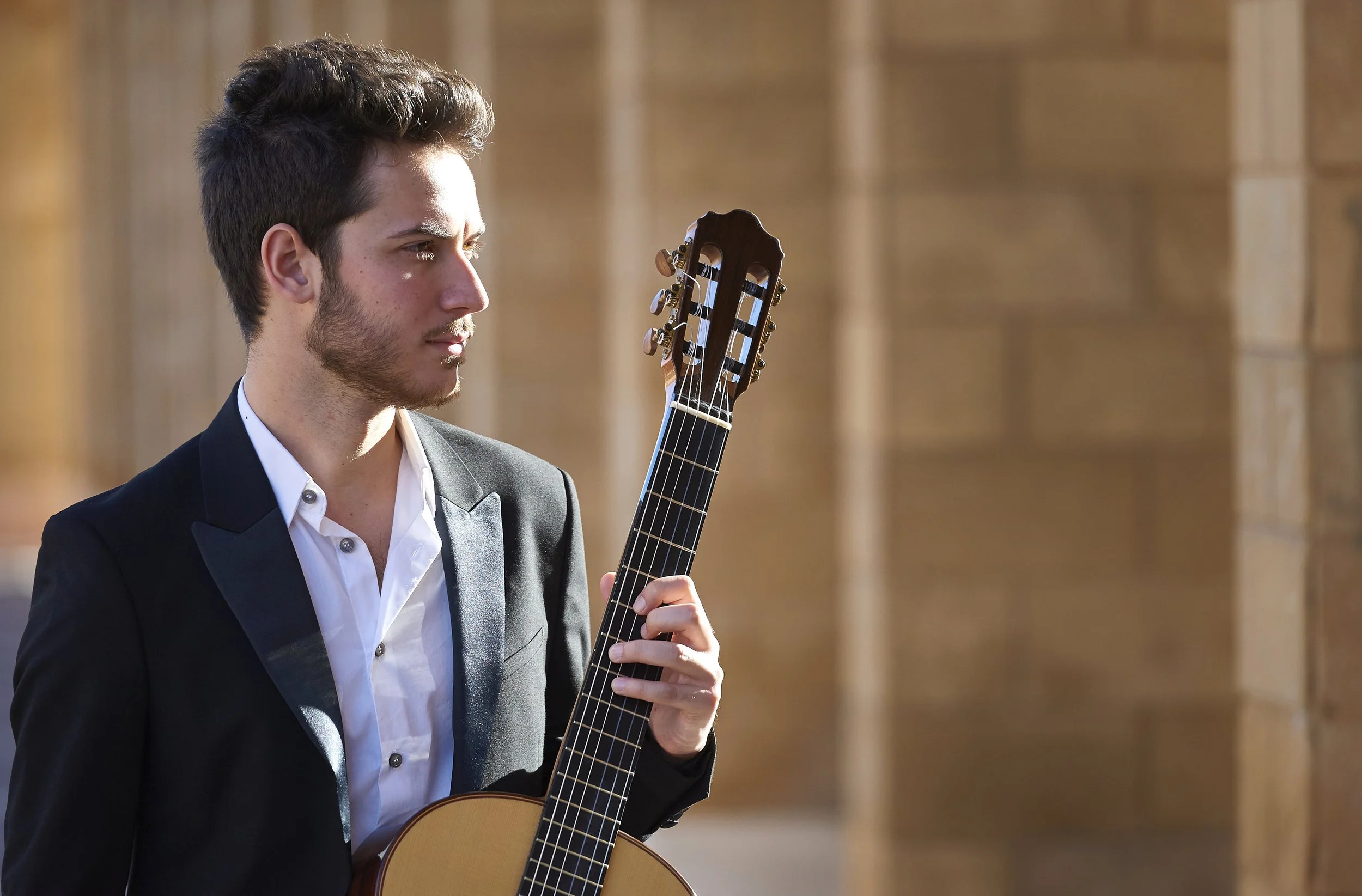 Giovane uomo in abito formale che suona una chitarra classica