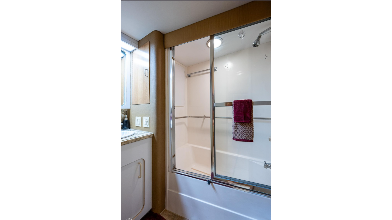 Bathroom with a shower that has a glass door, a towel hanging on a metal bar inside the shower, a small window, and a vanity with sink, granite countertop, and electrical outlets.