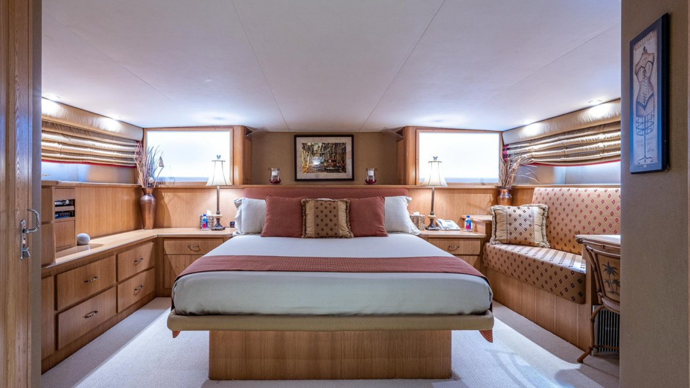 A hotel bedroom with a large bed, built-in wooden furniture, two windows, and lamps on each side of the bed.