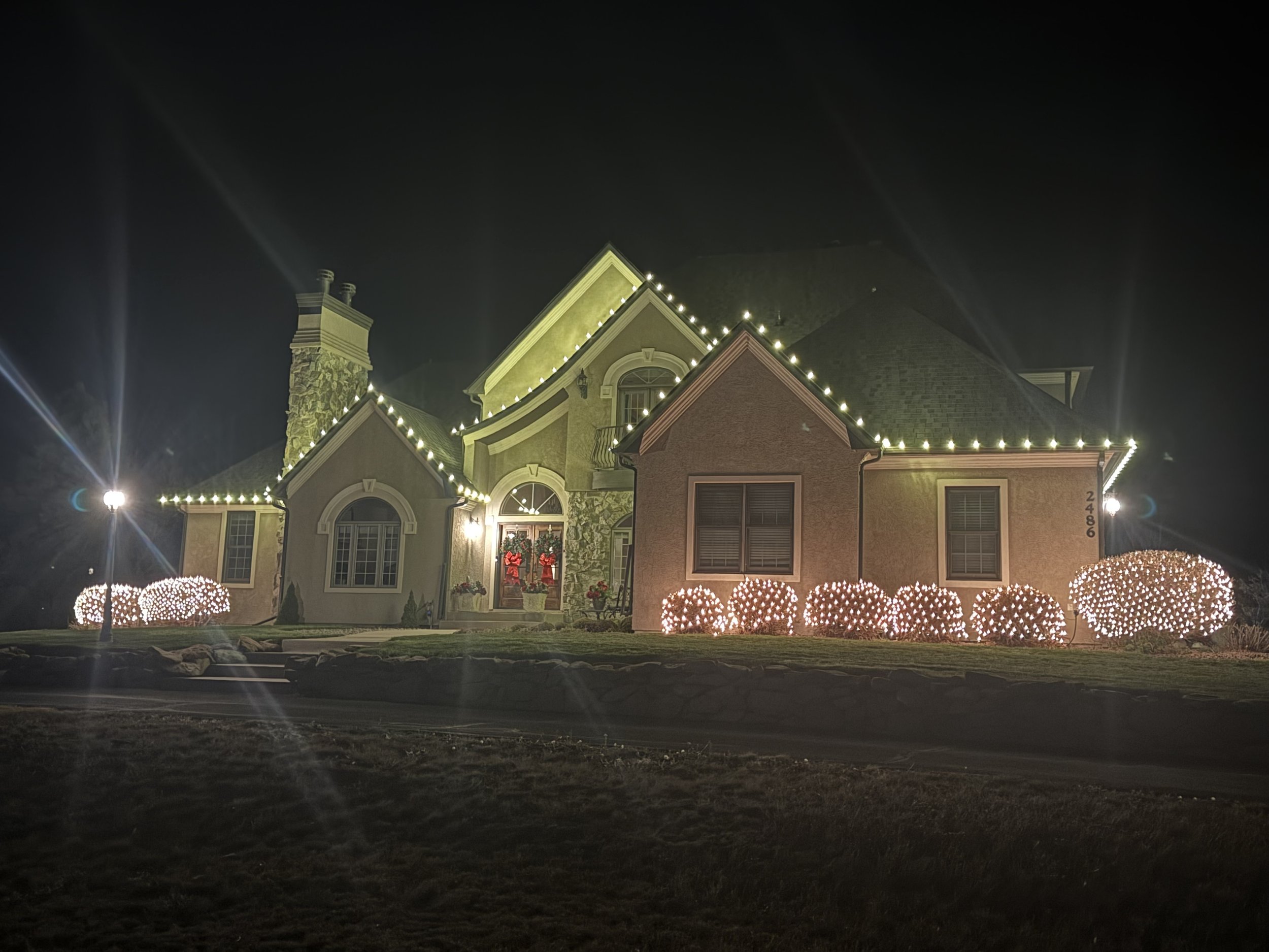 A large house decorated with Christmas lights at night, with trees wrapped in lights in the front yard.