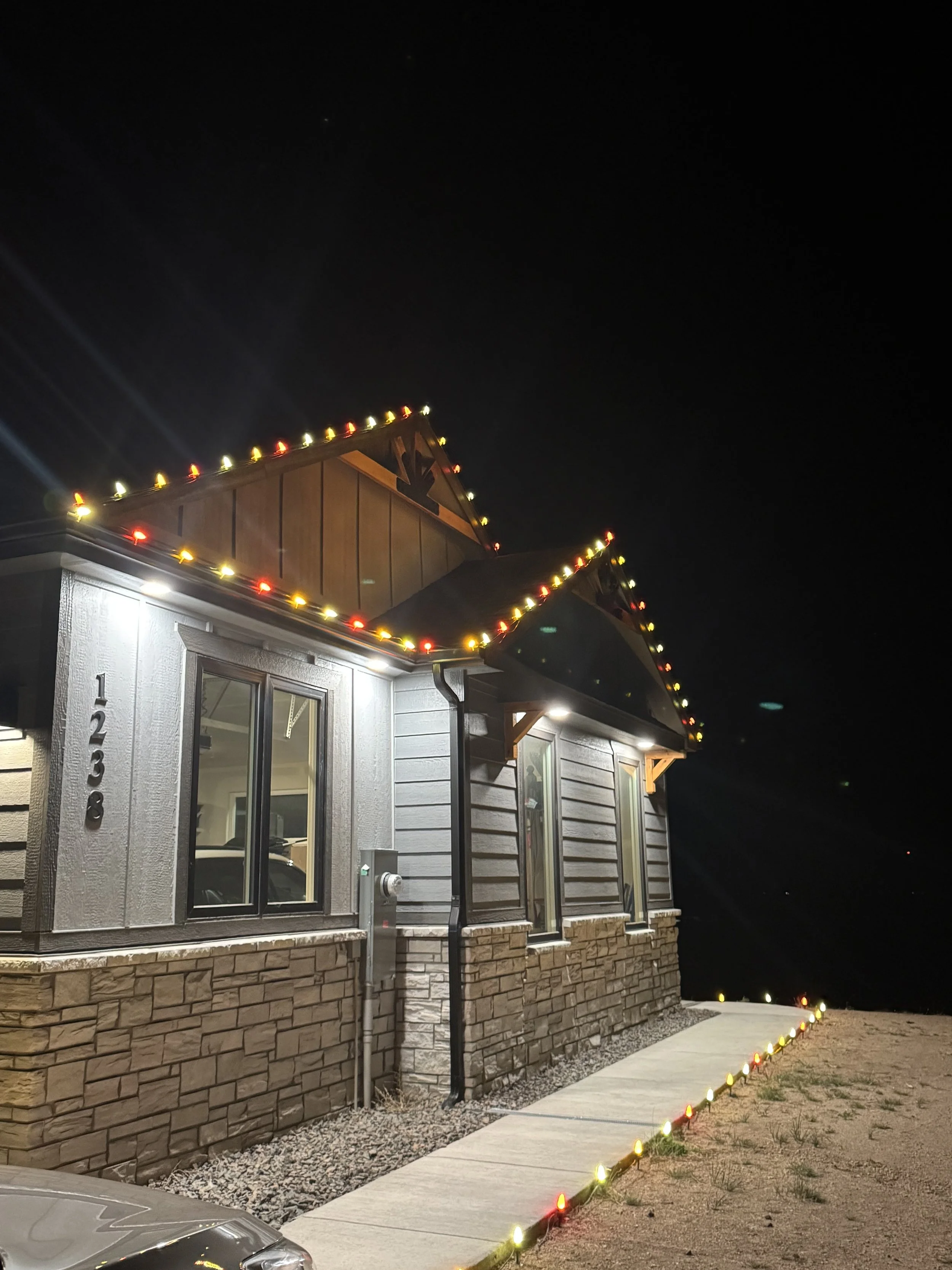 Front of a house at night decorated with Christmas lights along the roofline and walkway.