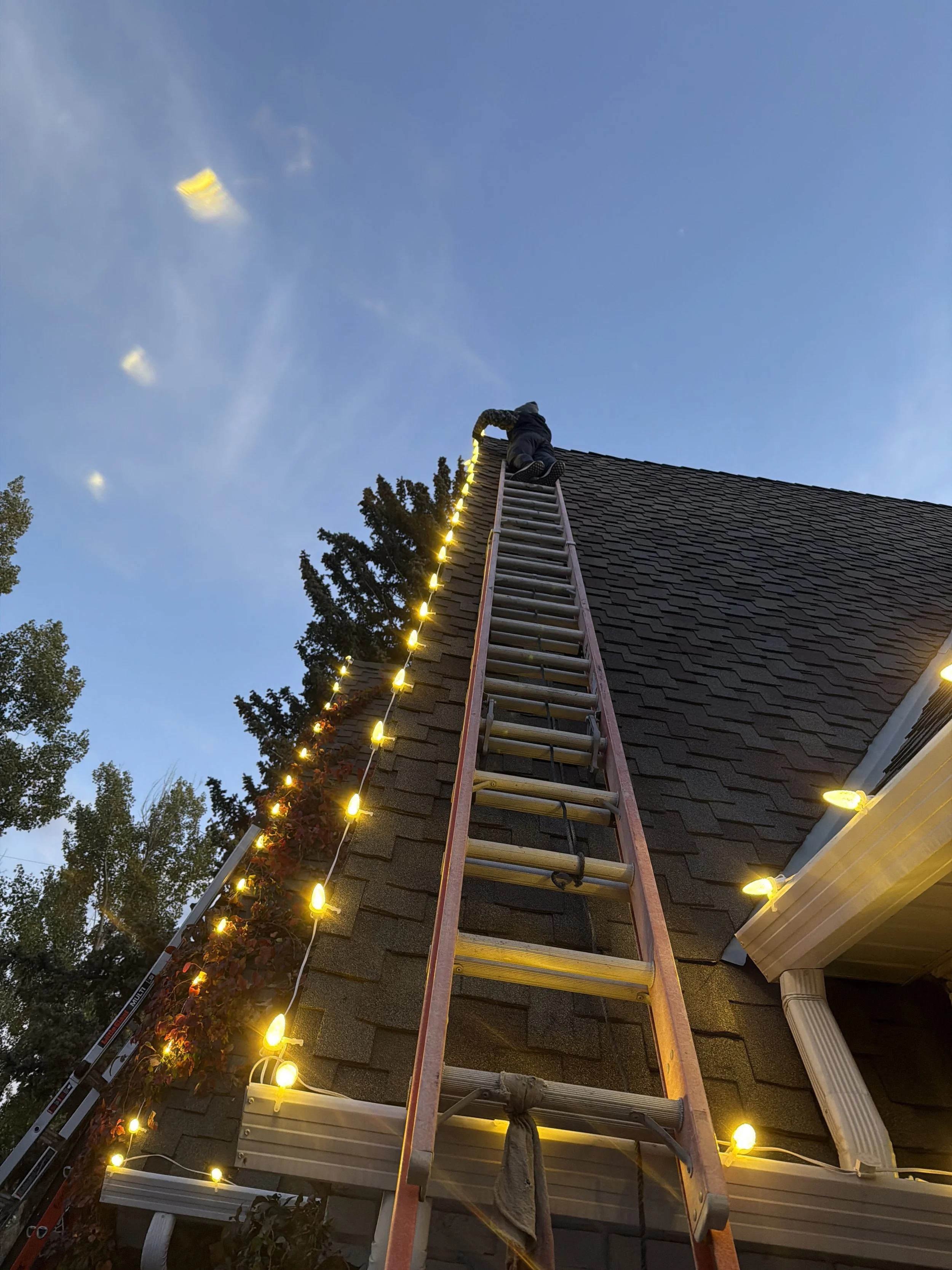 Christmas light installation technician on ladder decorating roofline, Cheyenne, WY