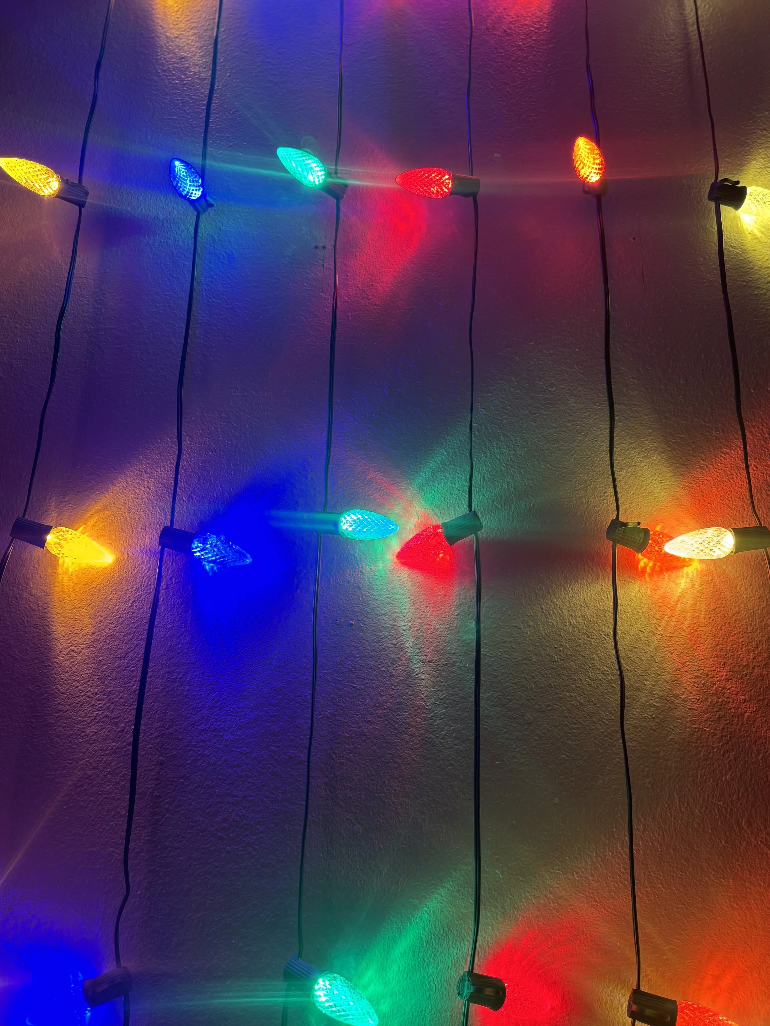 Colorful string lights hanging against a wall, casting reflections and shadows.