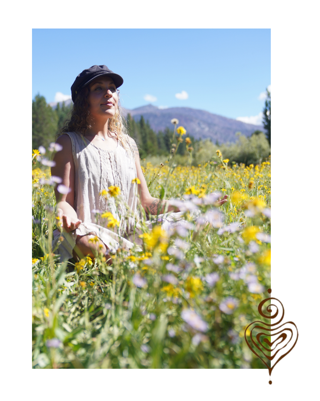 Woman sitting in a field of yellow and purple flowers with mountains and blue sky in the background.
