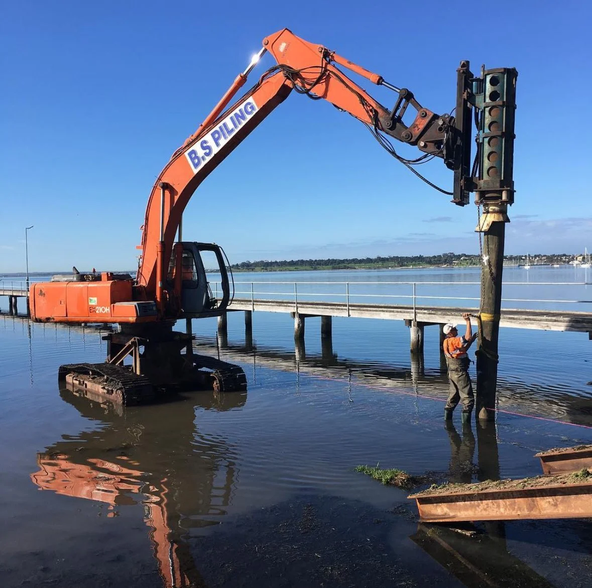 Construction worker using machinery to install or repair a pier or dock at a waterfront.