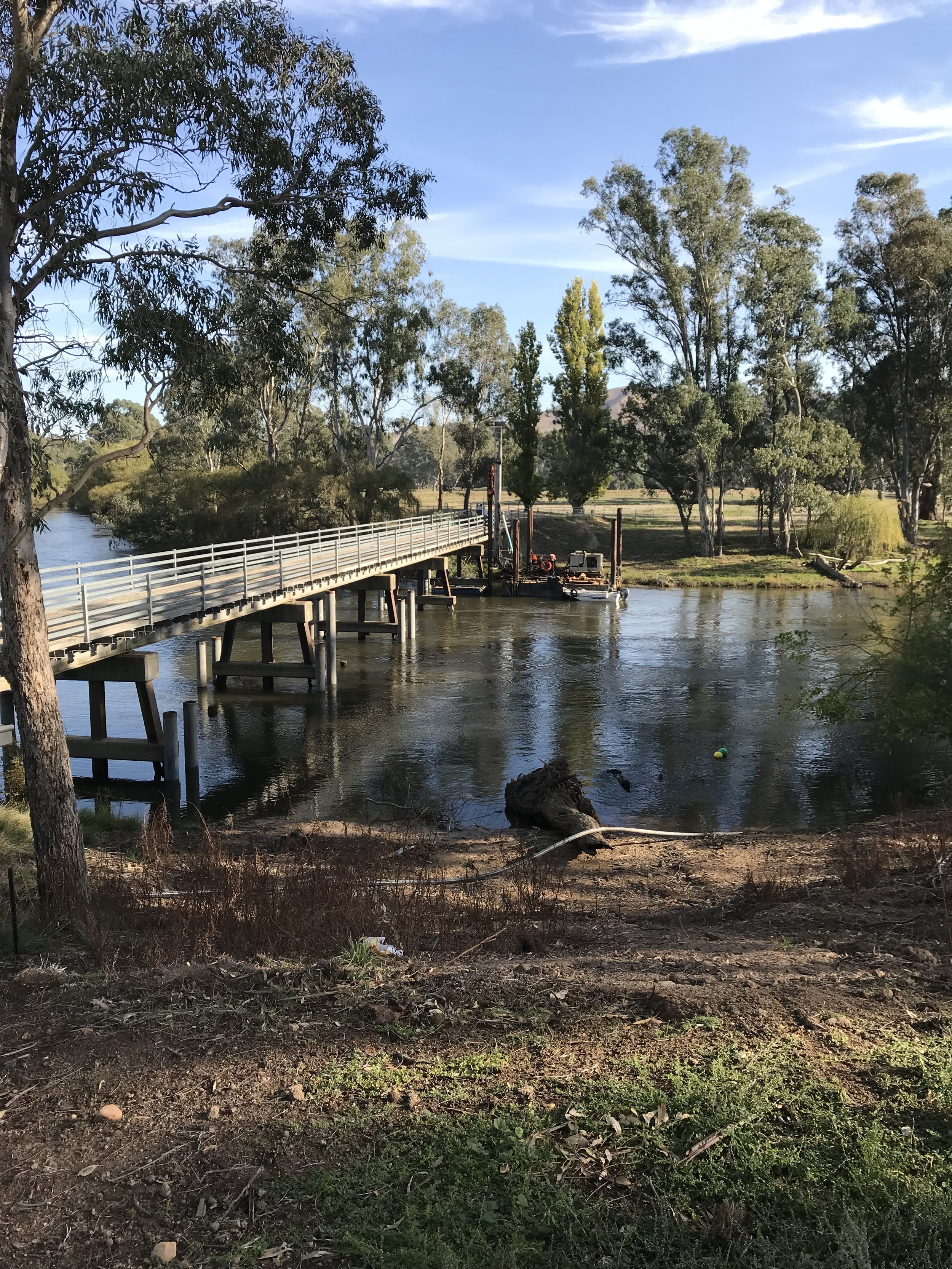 A river with a wooden bridge over it, surrounded by trees and greenery in a park-like setting on a clear day with blue skies.