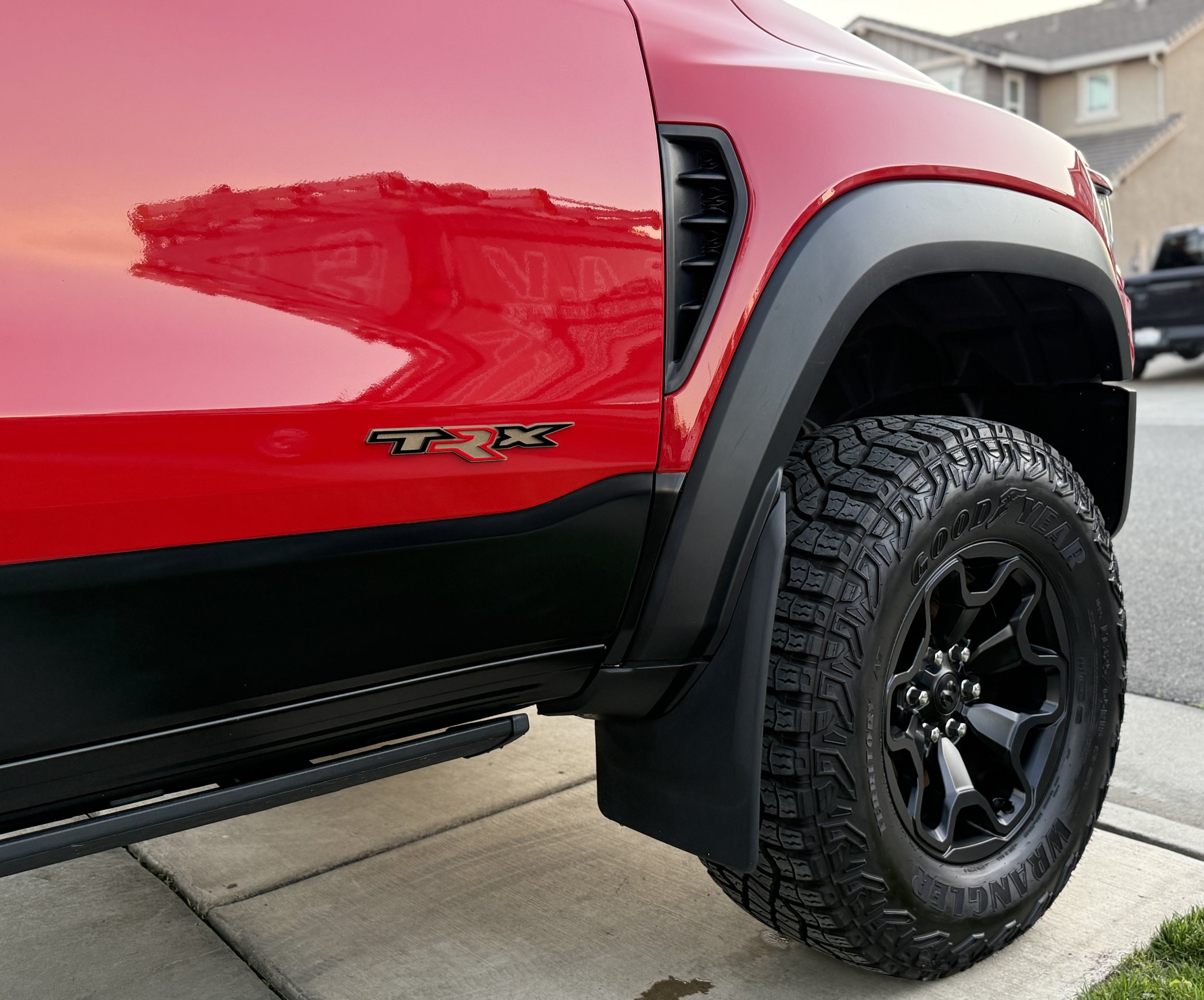 Close-up of a red pickup truck with a 'TRX' badge, showing an aggressive tire and black wheel on a residential driveway during sunset.