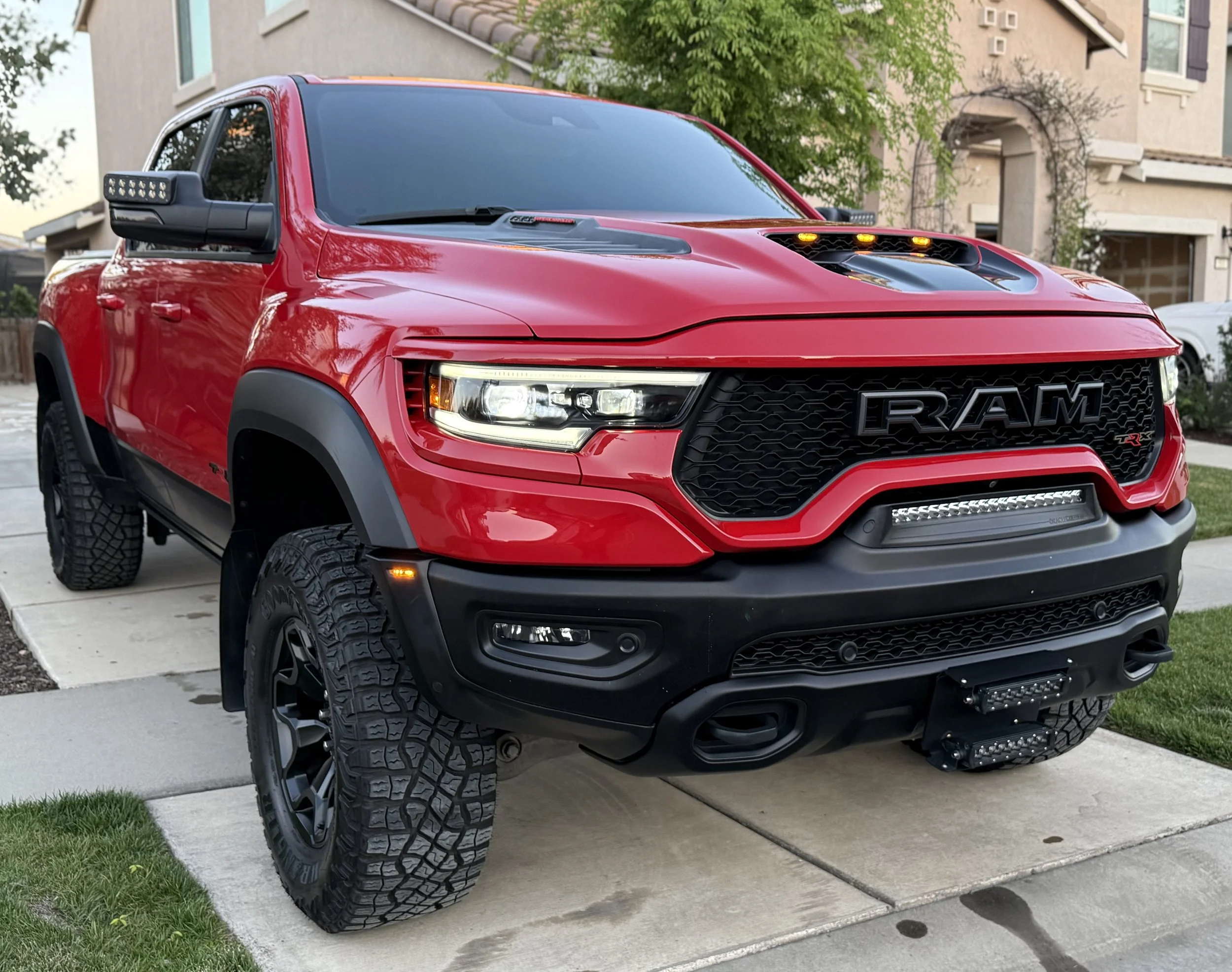 Red RAM truck with black grille and off-road tires parked on a driveway in front of a house.