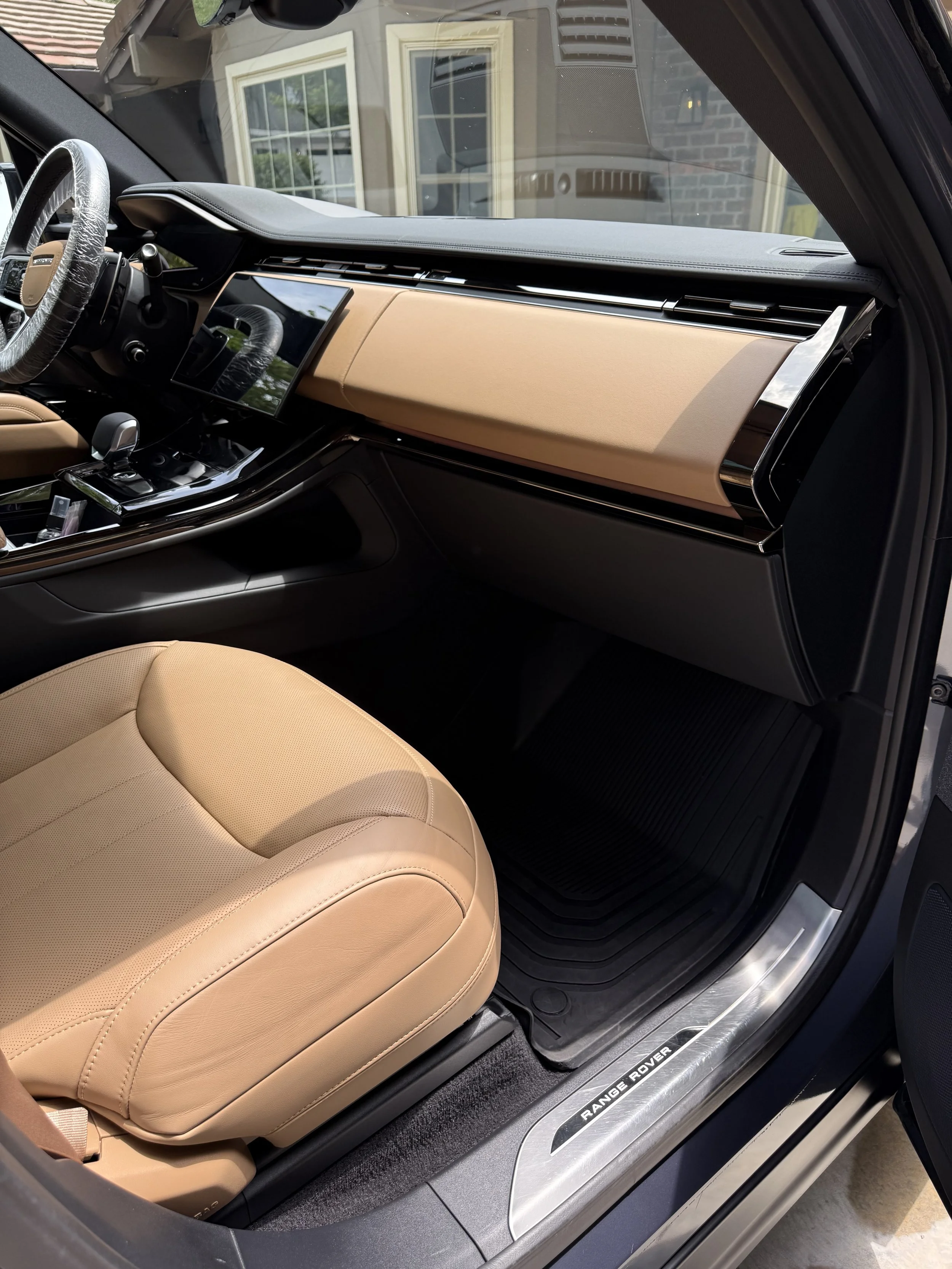 The interior of a Range Rover vehicle, showcasing a tan leather seat, a dashboard with a digital display, and the Range Rover logo on the door sill.