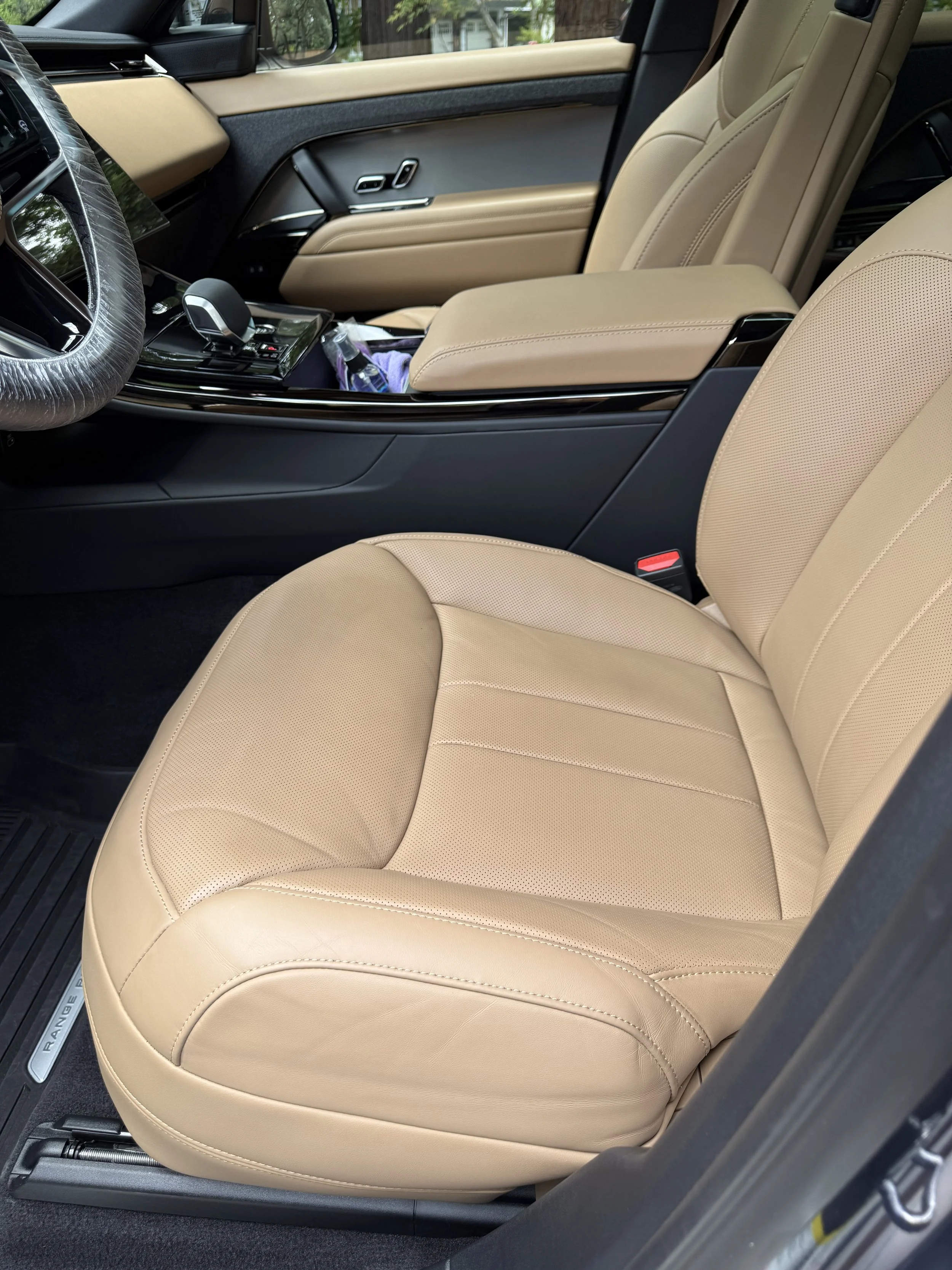 Interior of a vehicle, showing beige leather seats, a center armrest, and a dashboard with controls.