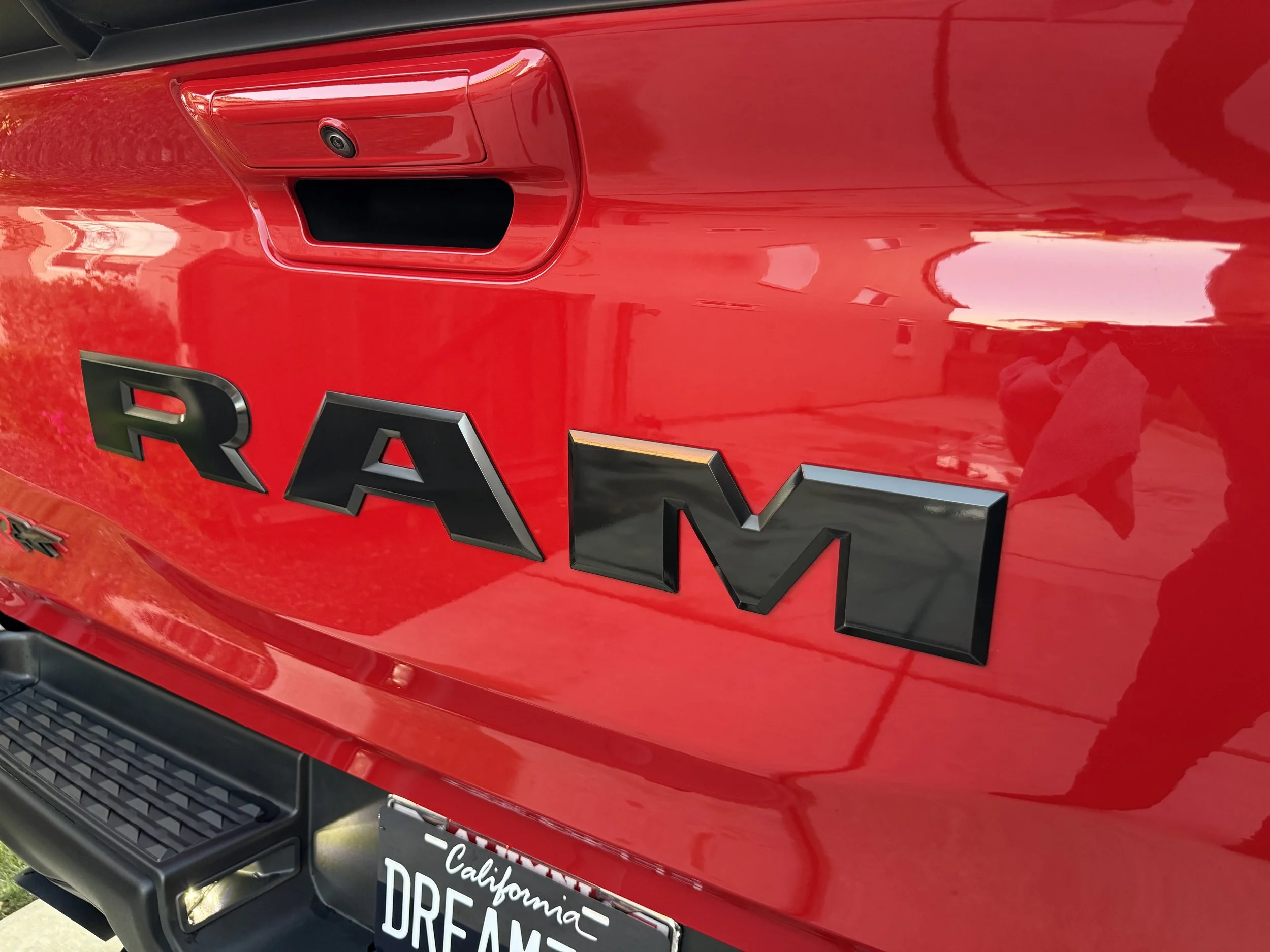 Close-up of a red RAM truck with the RAM logo in black letters on the tailgate, and a California license plate that reads "DREAM".