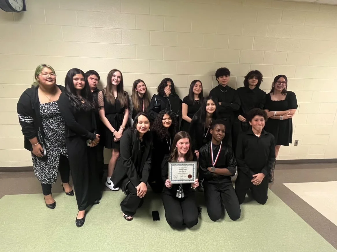 Group of young people, some holding certificates and medals, posing indoors against a yellow wall.