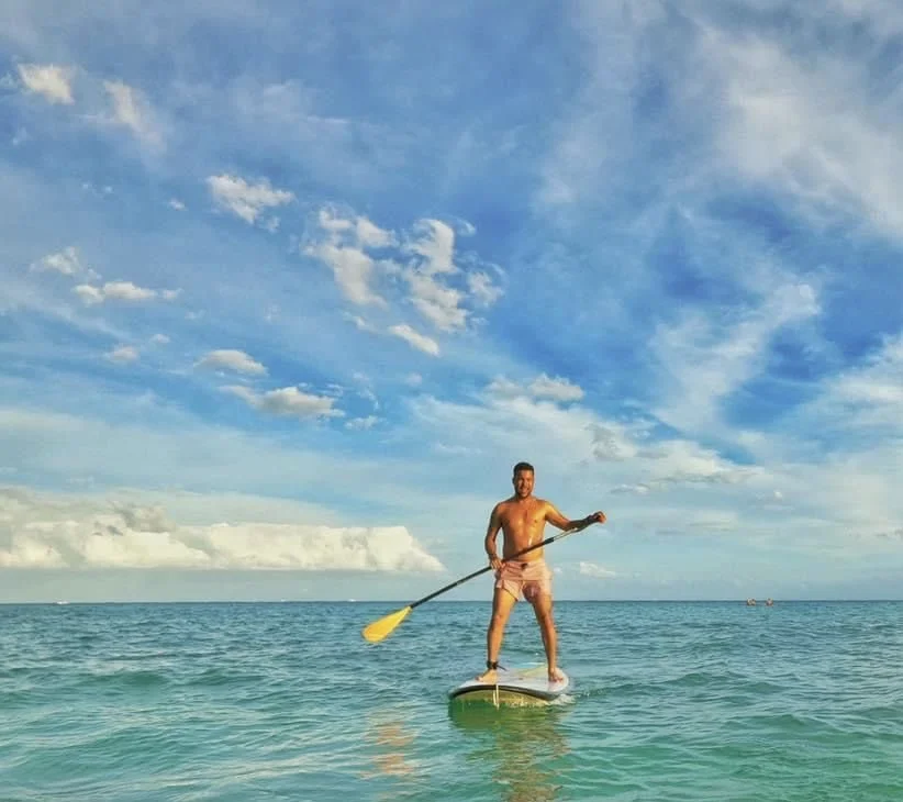 Romano Theunissen paddleboarding in the ocean with a blue sky and scattered clouds overhead.