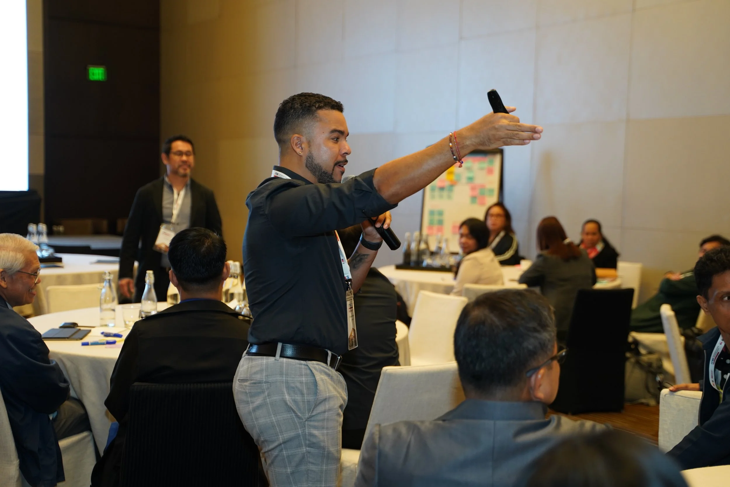 Romano Theunissen holding a microphone and a remote control, speaking at a strategic foresight workshop, with audience members from the Philippines government, private sector and civil service,  seated at tables in the background.