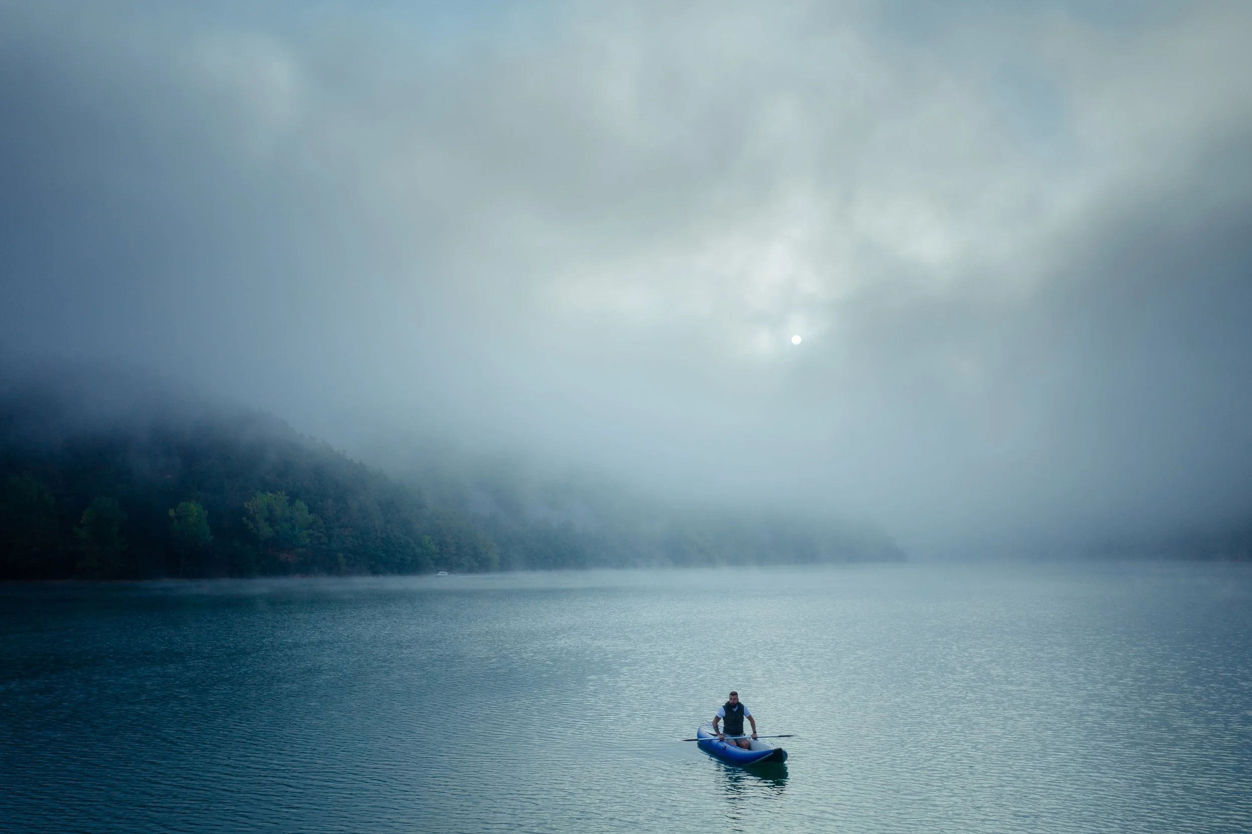man-paddling-in-foggy-mountain-lake-by-forest