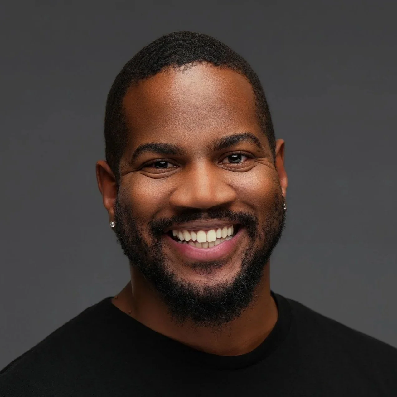 A young man with short hair and a mustache, wearing a white shirt, blue striped tie, and a dark patterned scarf, posing indoors with a neutral expression.