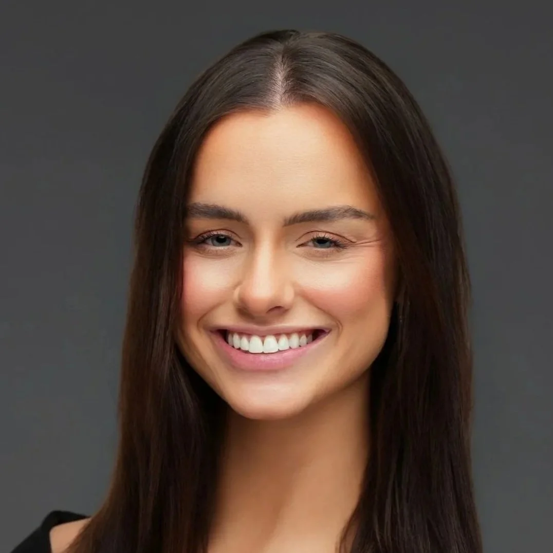 A young woman with long dark hair smiling against a gray background.