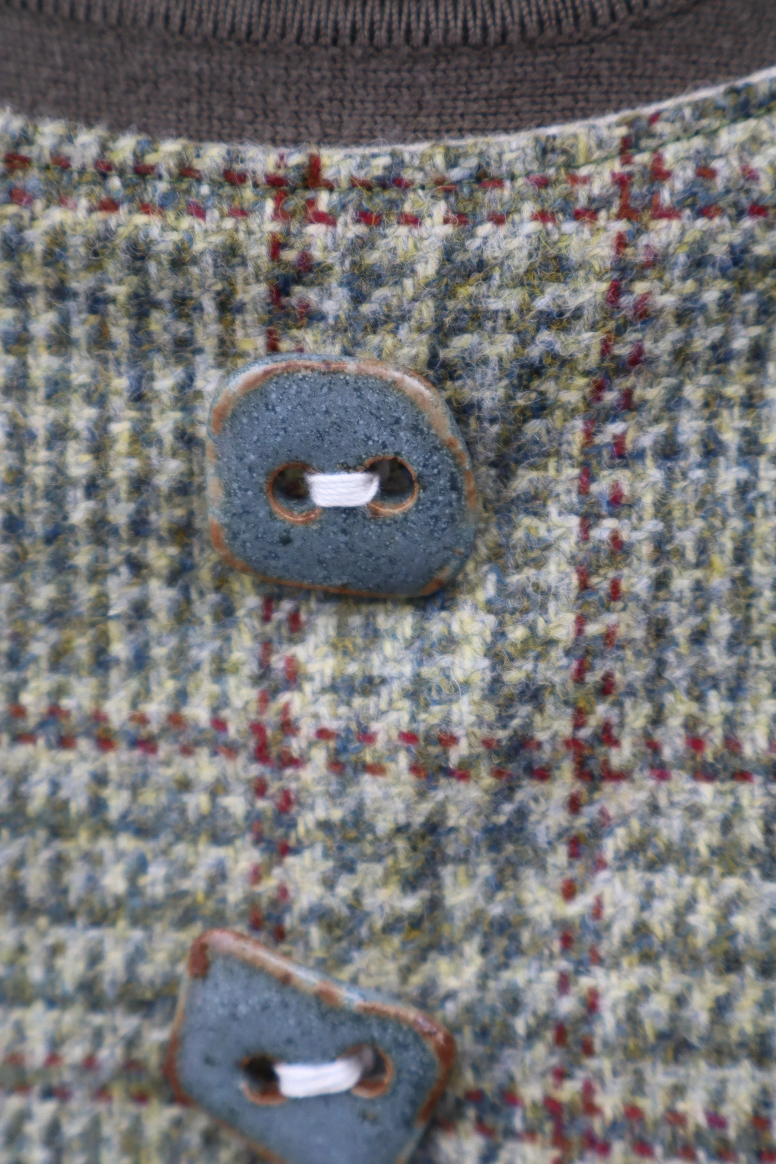 Close up of a turquoise clay button on a multicolored wool jacket. Item is medieval inspired and historically influenced