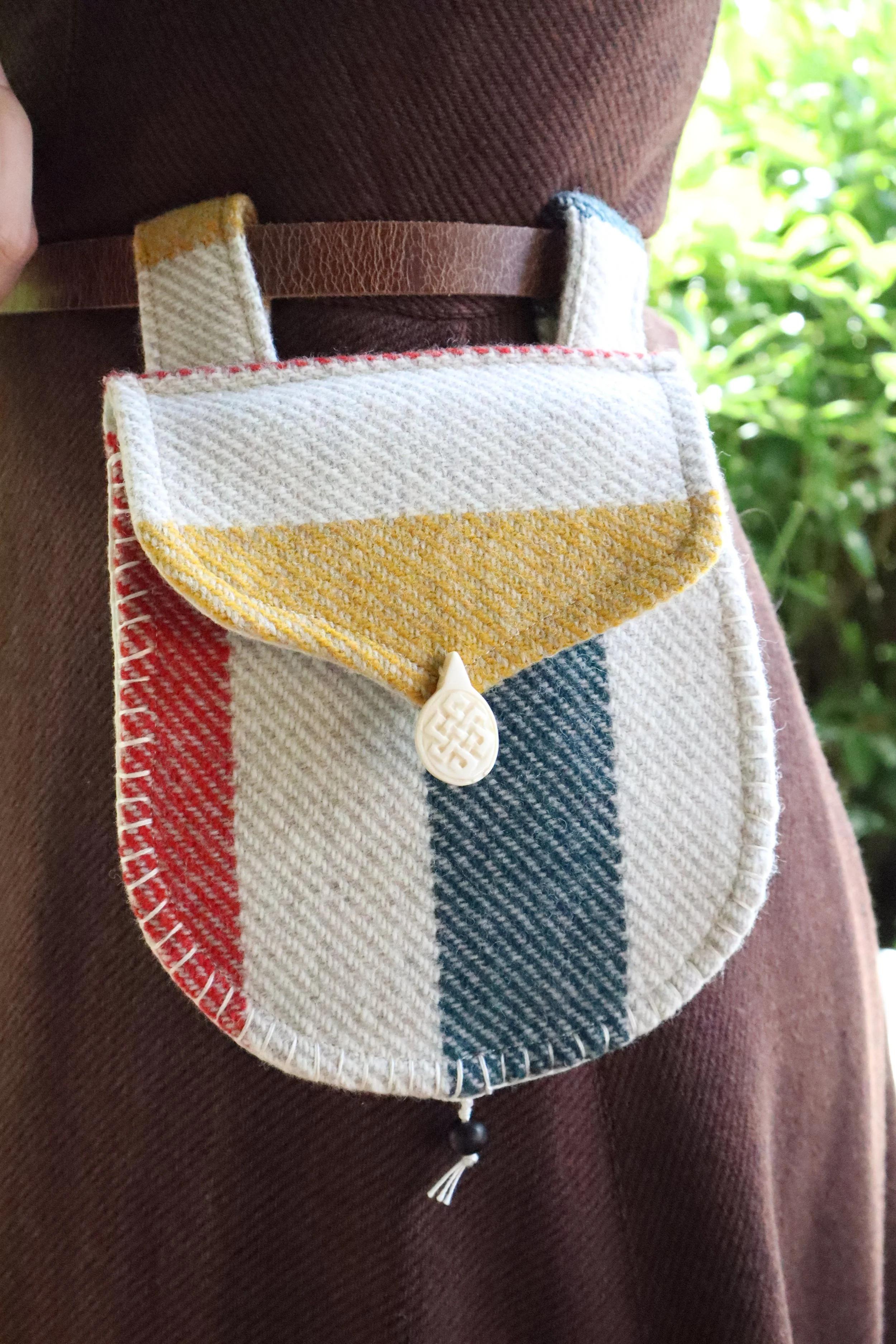 Tan and multicolor Wool Bag with bone clasp with brown background on a person's belt