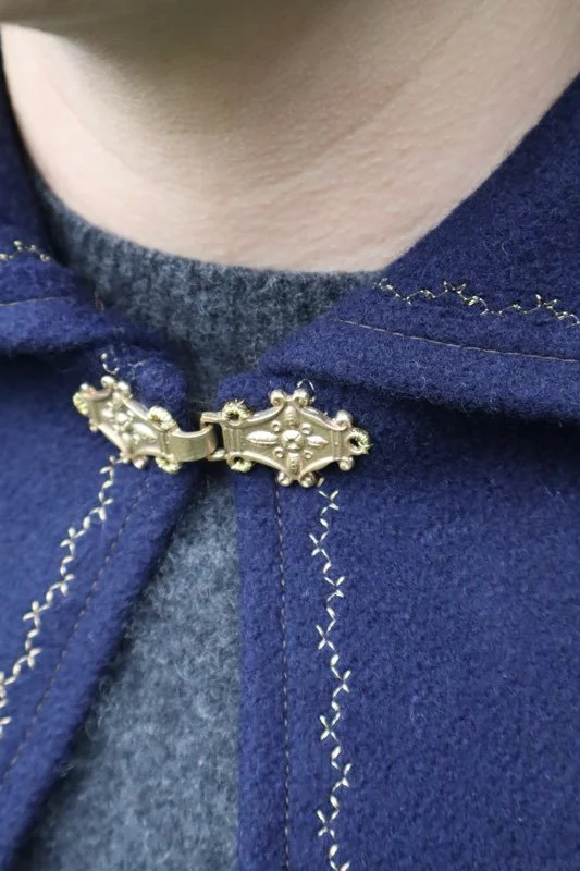 Close-up of a person wearing a blue woolen capelet with decorative clasp over a gray shirt.