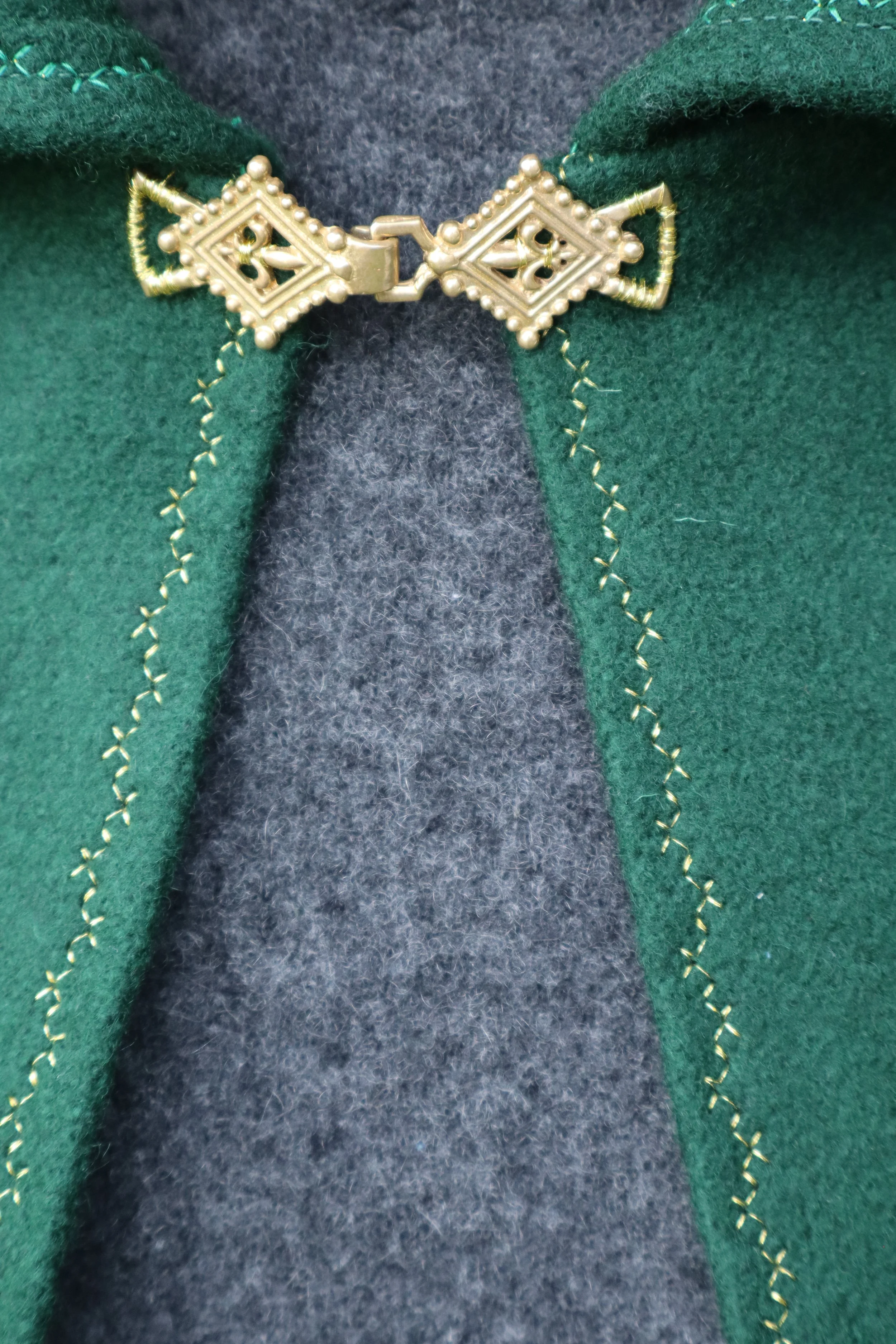 Close up of a gold metal clasp attached to a green fabric cloak.