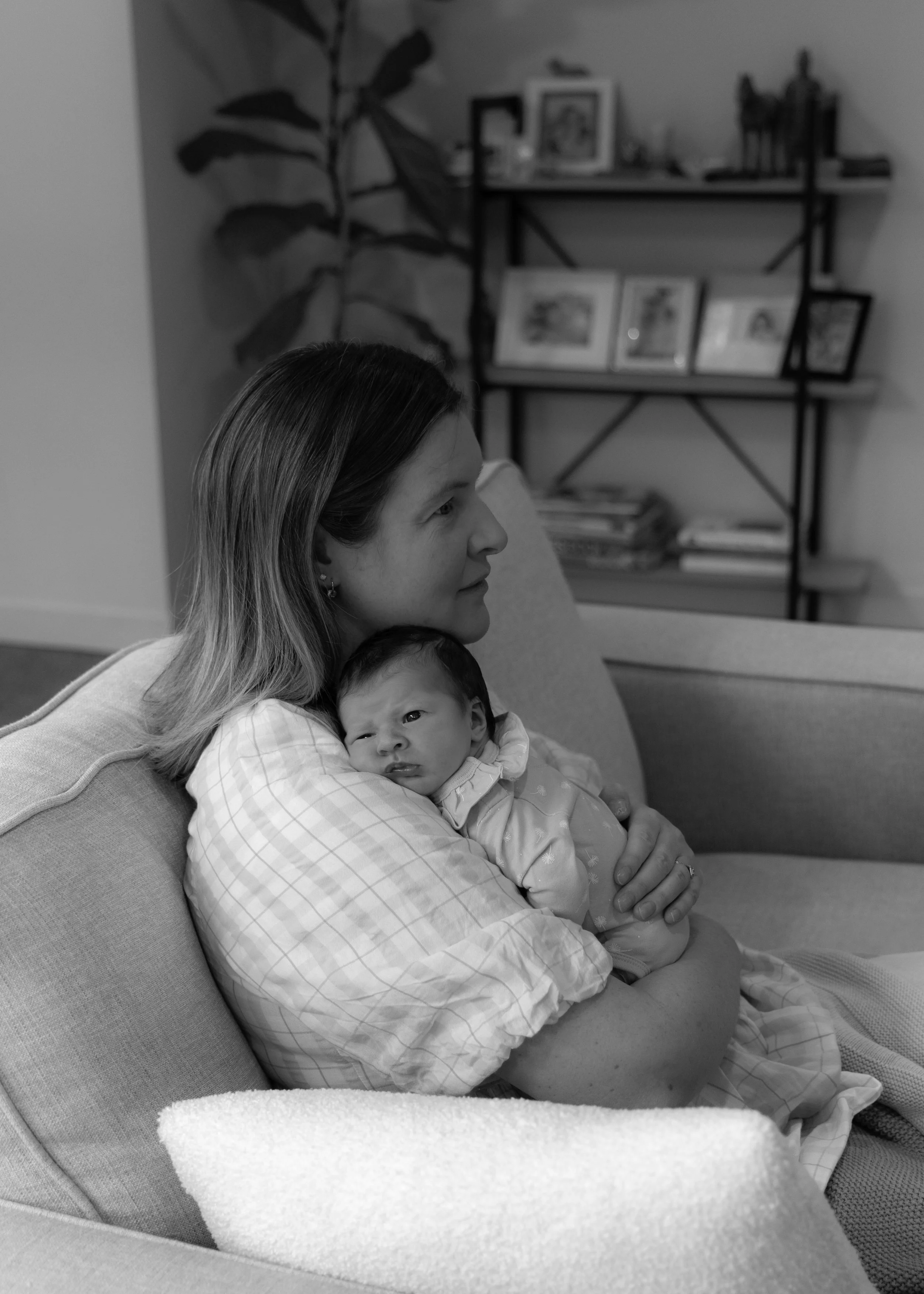 mum sitting on the couch cuddling newborn daughter at home