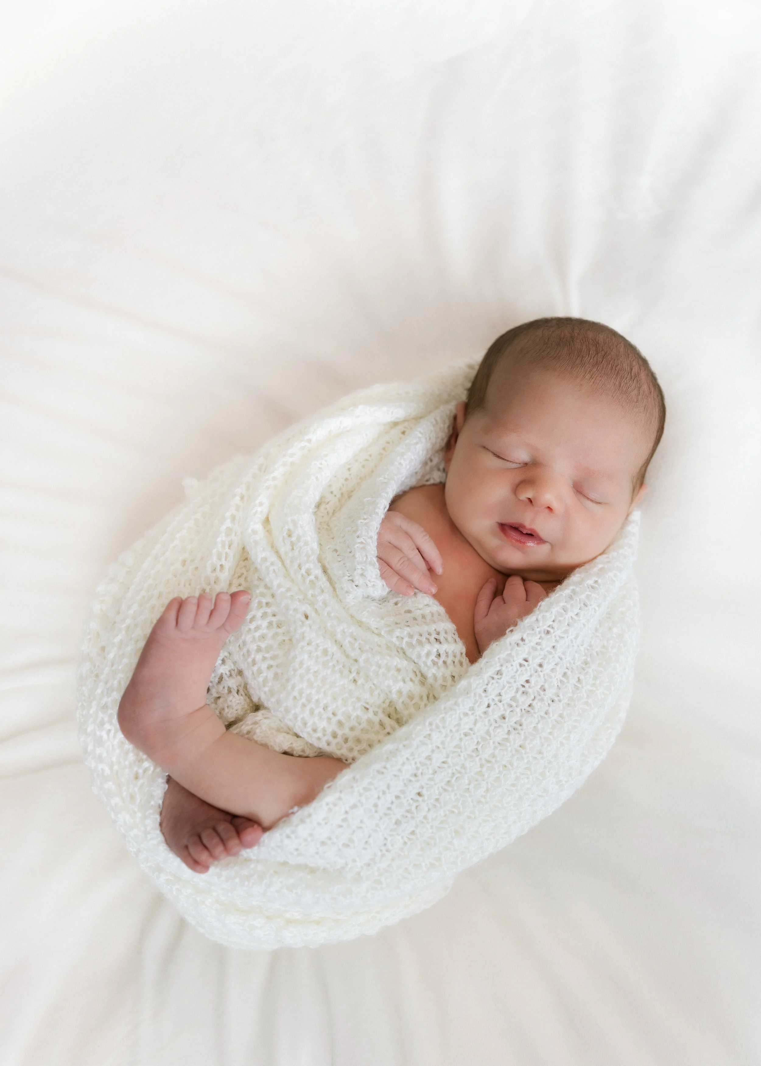 sleeping newborn swaddled peacefully in knit white blanket