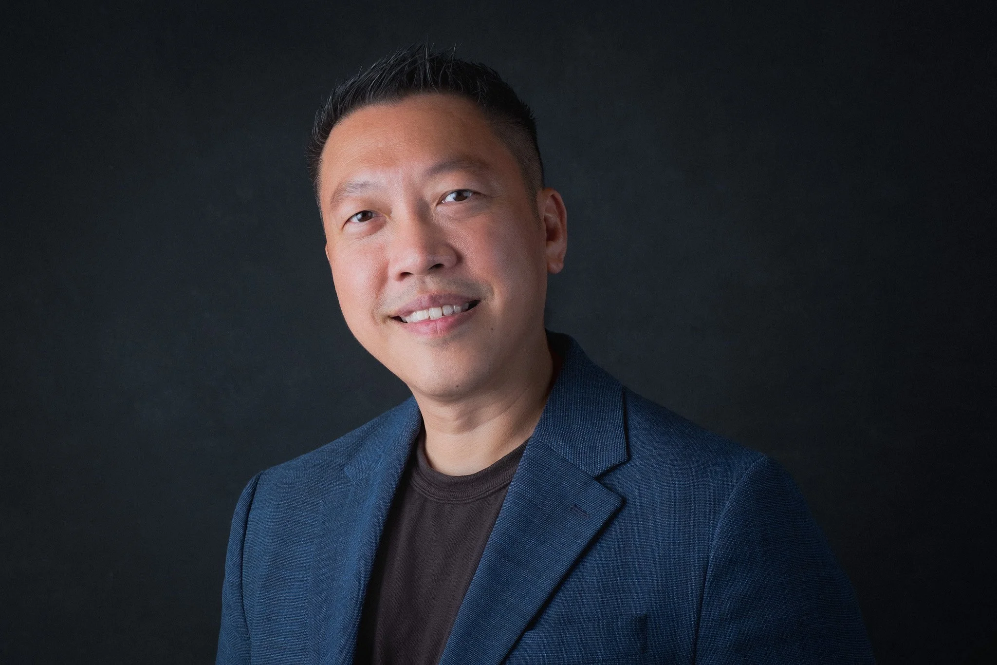 Studio portrait of a business leader smiling confidently against a dark background for speaker profiles, executive headshots and professional branding.